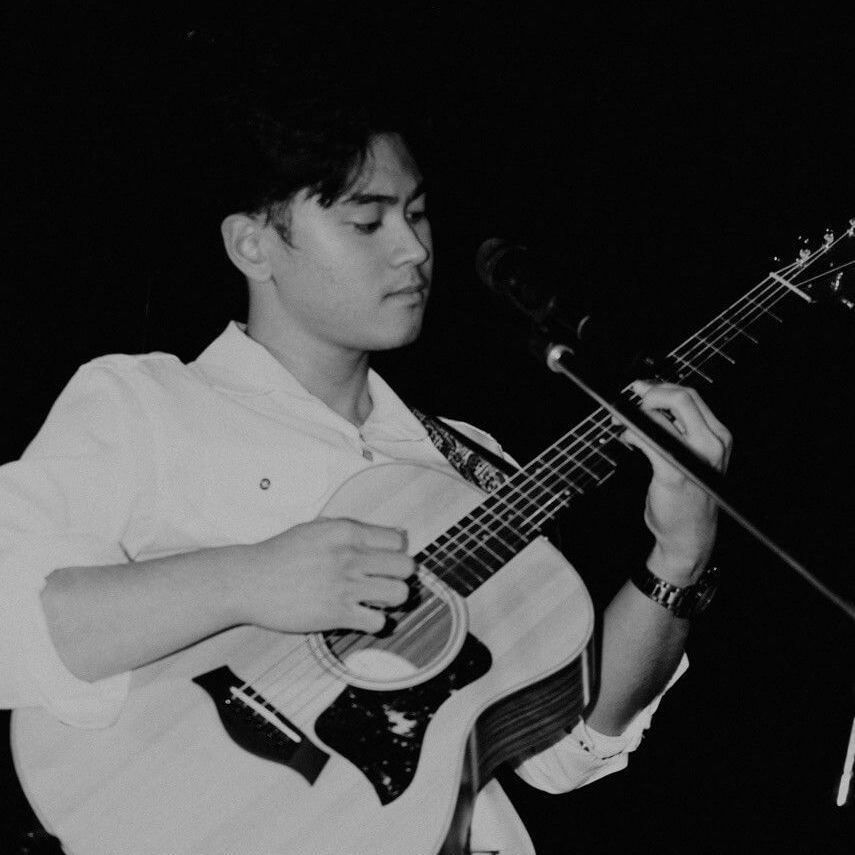 Man playing an acoustic guitar with a microphone in a dim setting.