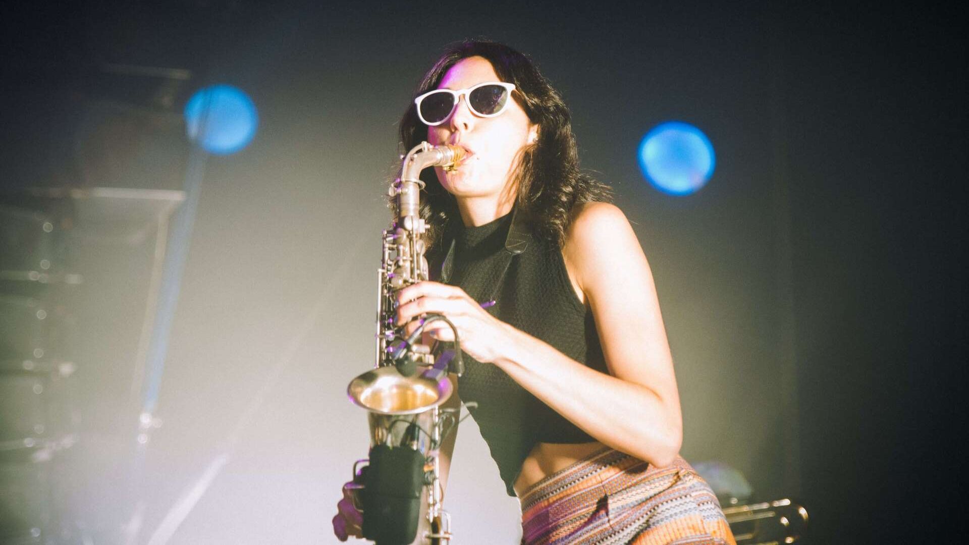 A woman wearing sunglasses is playing a saxophone on a stage.