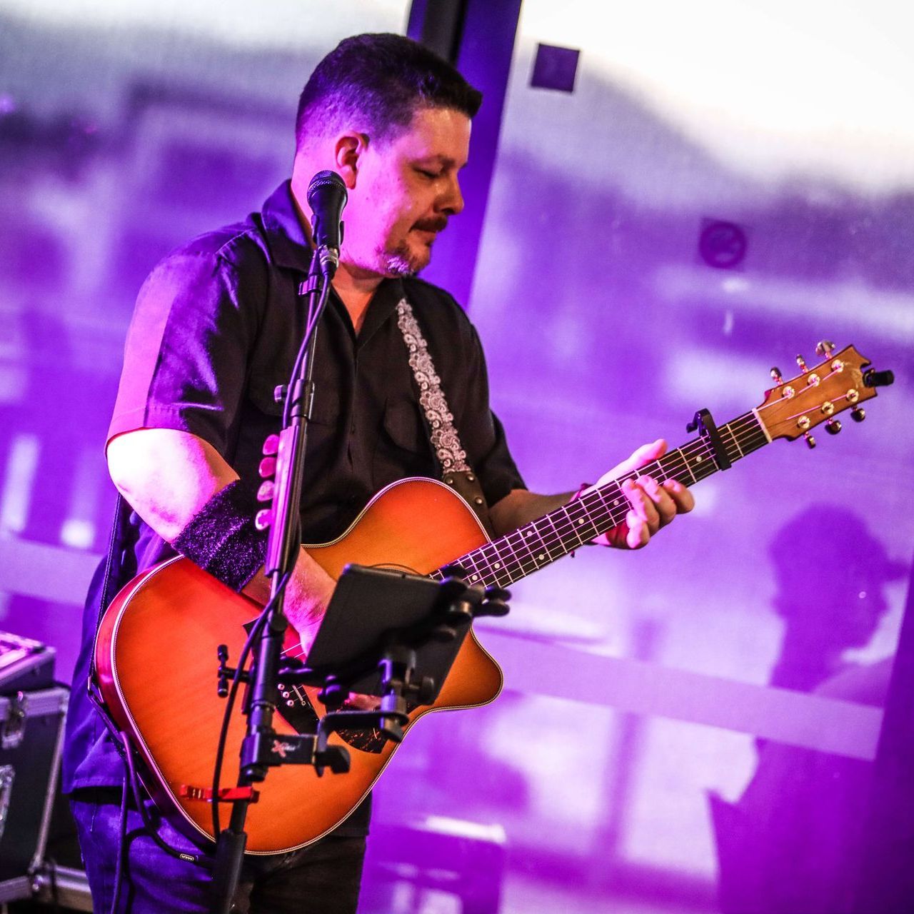 Man playing guitar and singing into a microphone. Purple lighting, indoors.