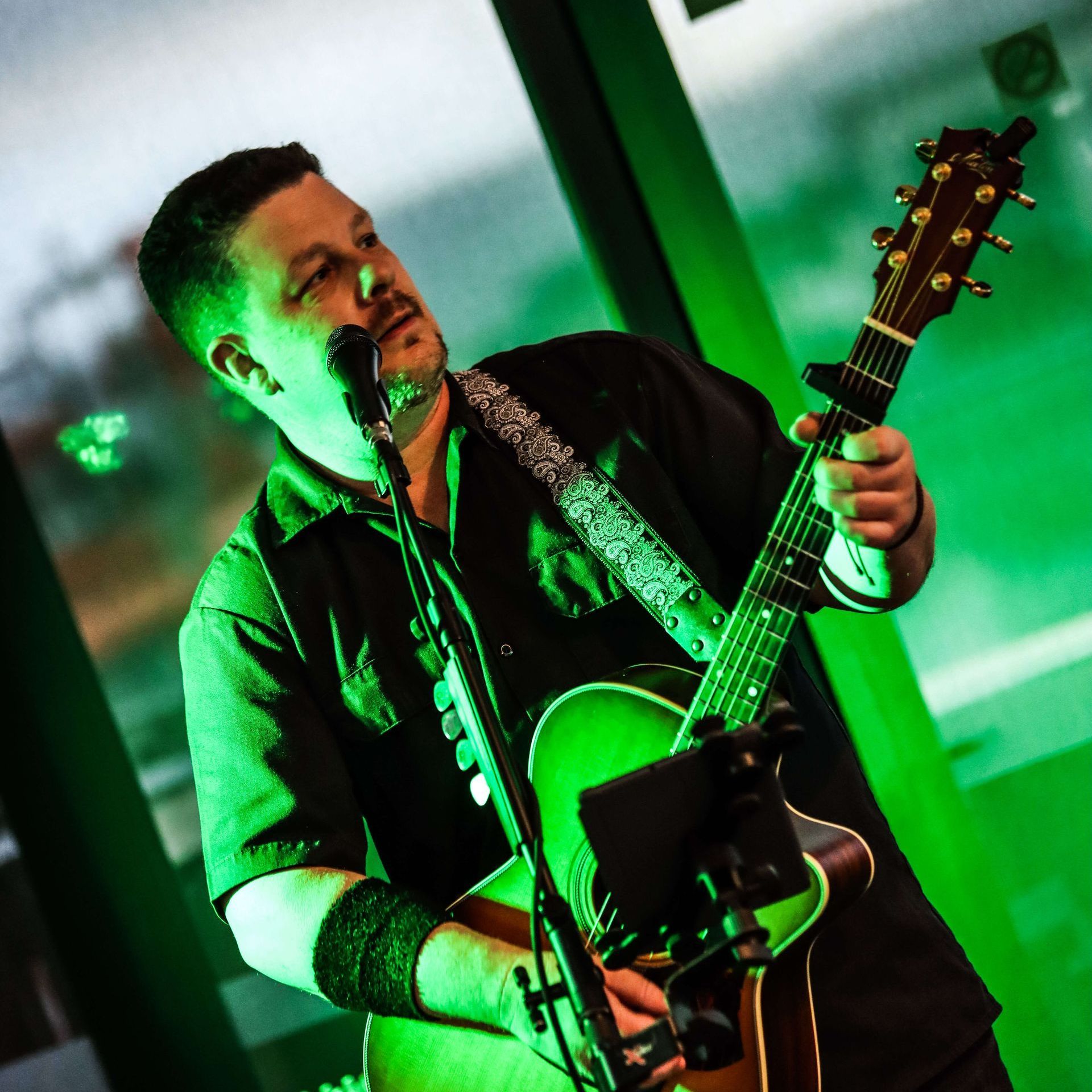Man singing and playing acoustic guitar, lit with green light.