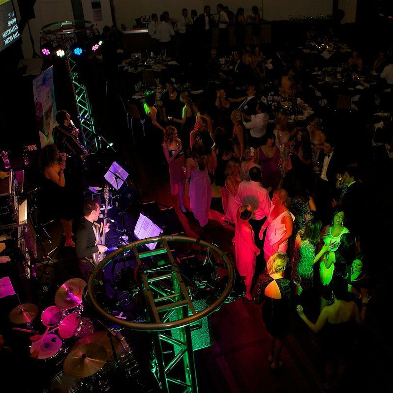 People dancing at a formal event, lit by colorful stage lights and a band playing on a stage.