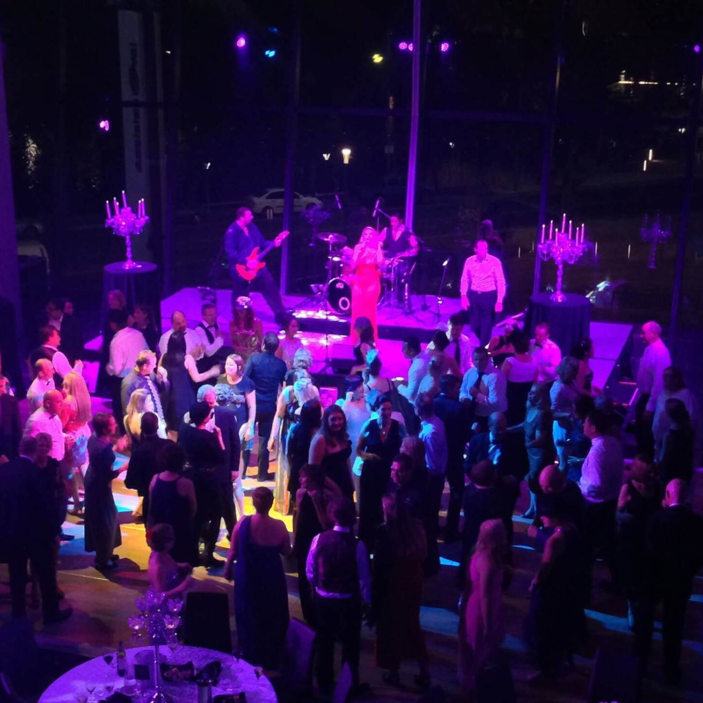 People dancing at a party with a band on stage, lit with purple and white lights.