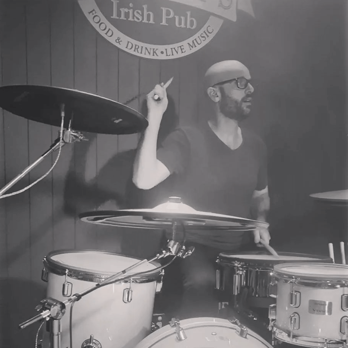 A musician playing drums in an Irish pub, captured in a black-and-white, dimly lit shot.