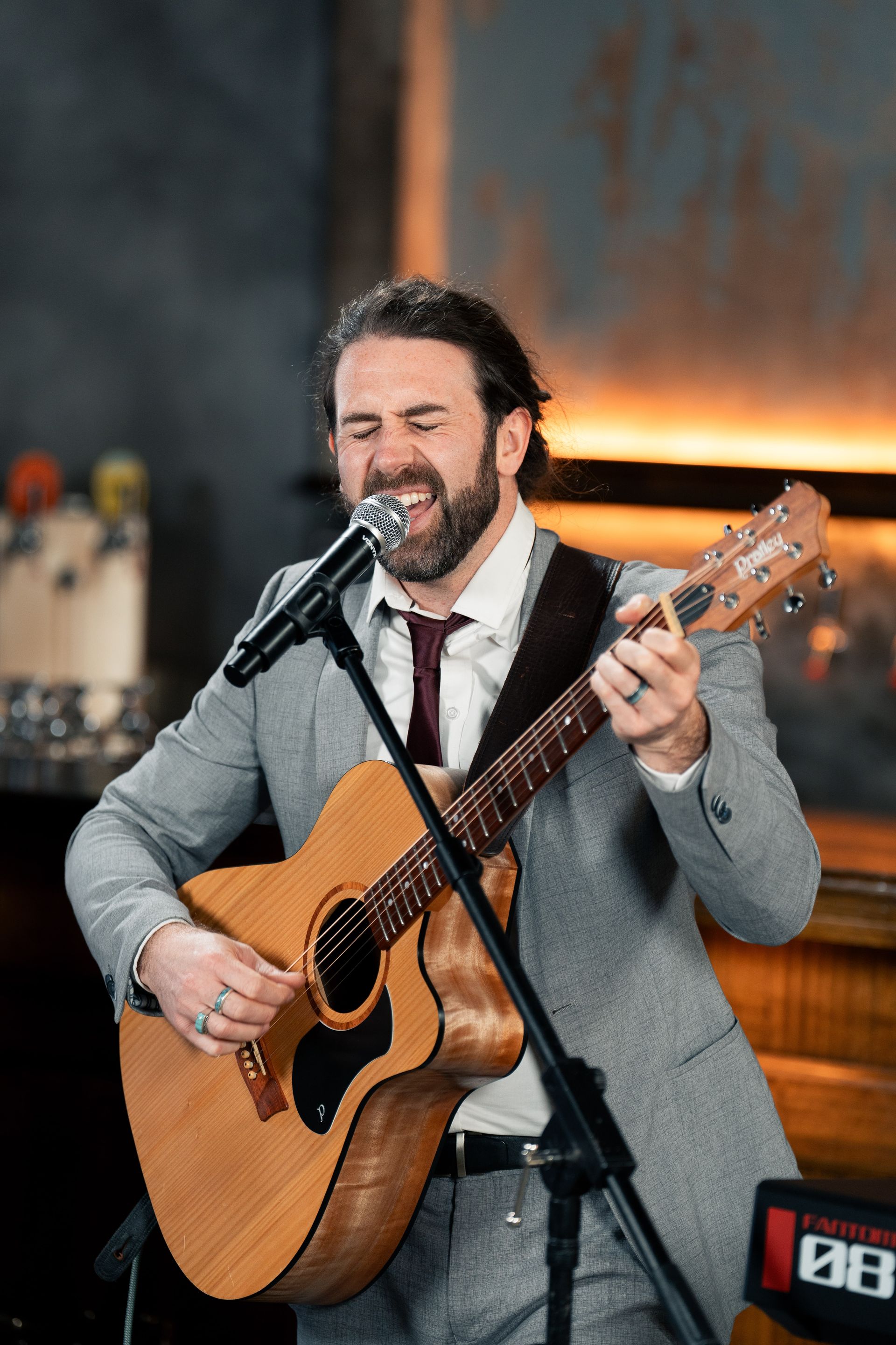 Man in a gray suit plays acoustic guitar and sings into a microphone.