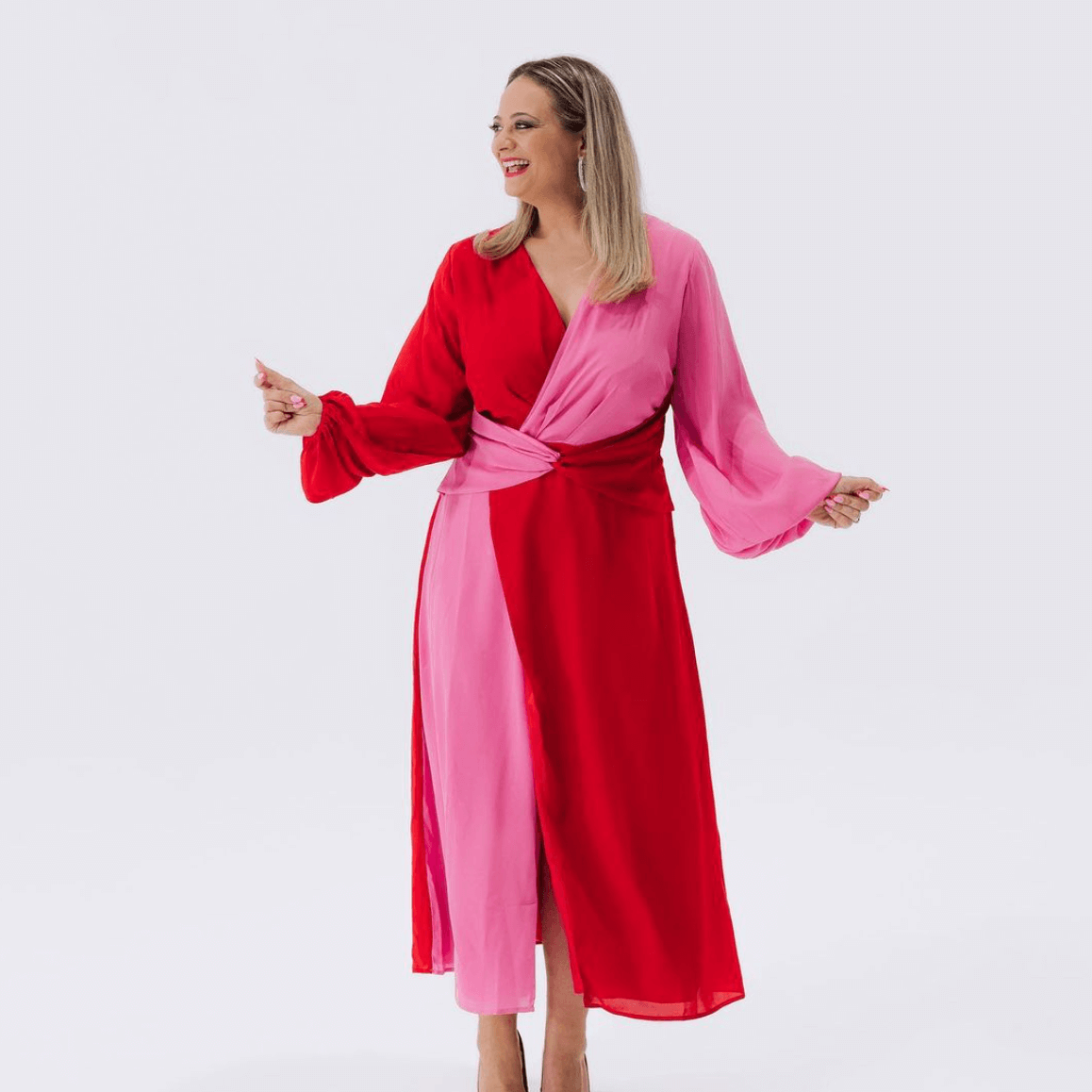 Woman in a red and pink color-block dress, smiling and posing.