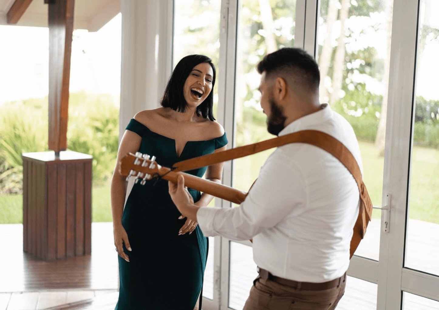Man serenading a smiling woman with a guitar in a bright indoor space