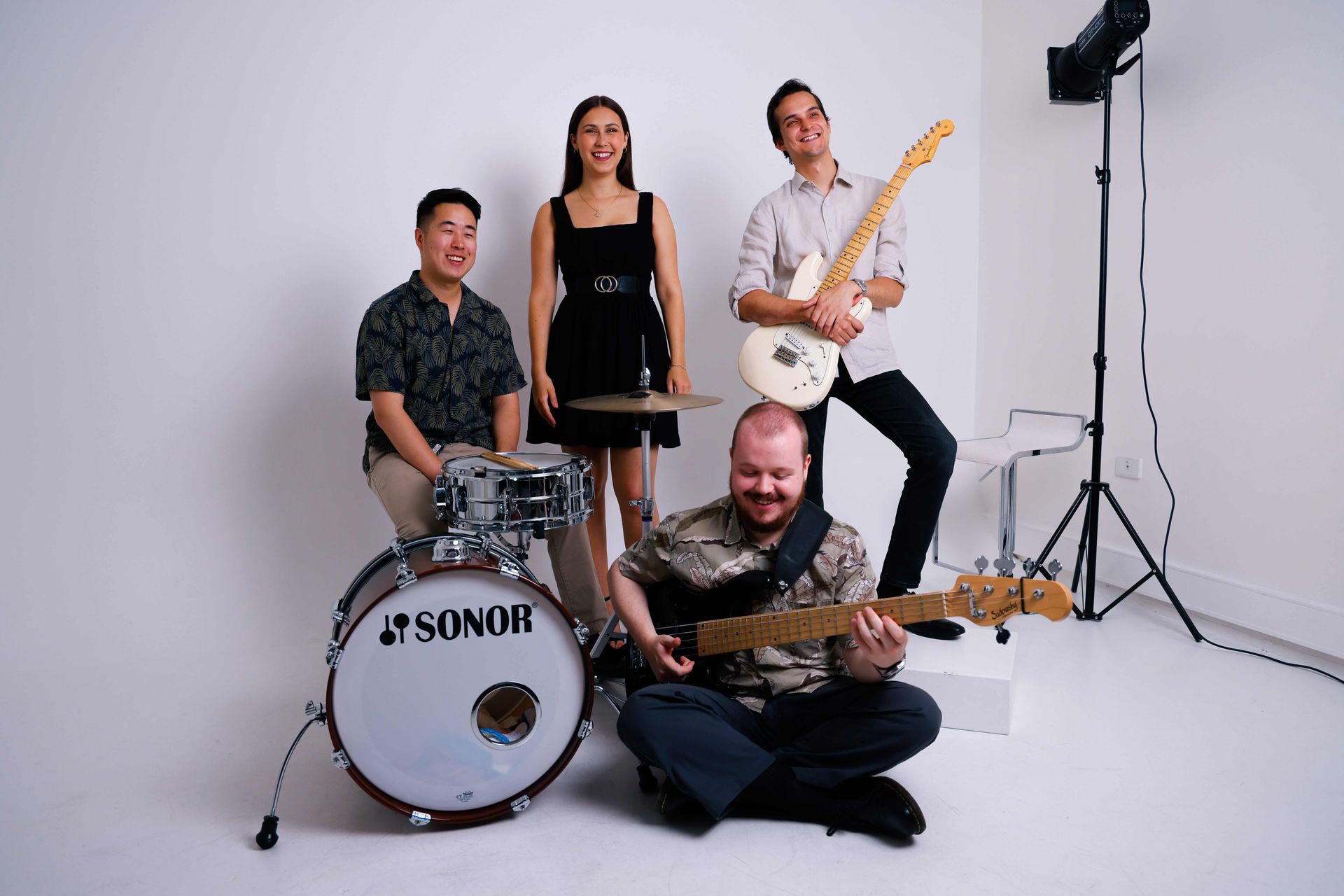 Four band members in a studio setting, with a drummer, bassist, and two guitarists posing with their instruments.