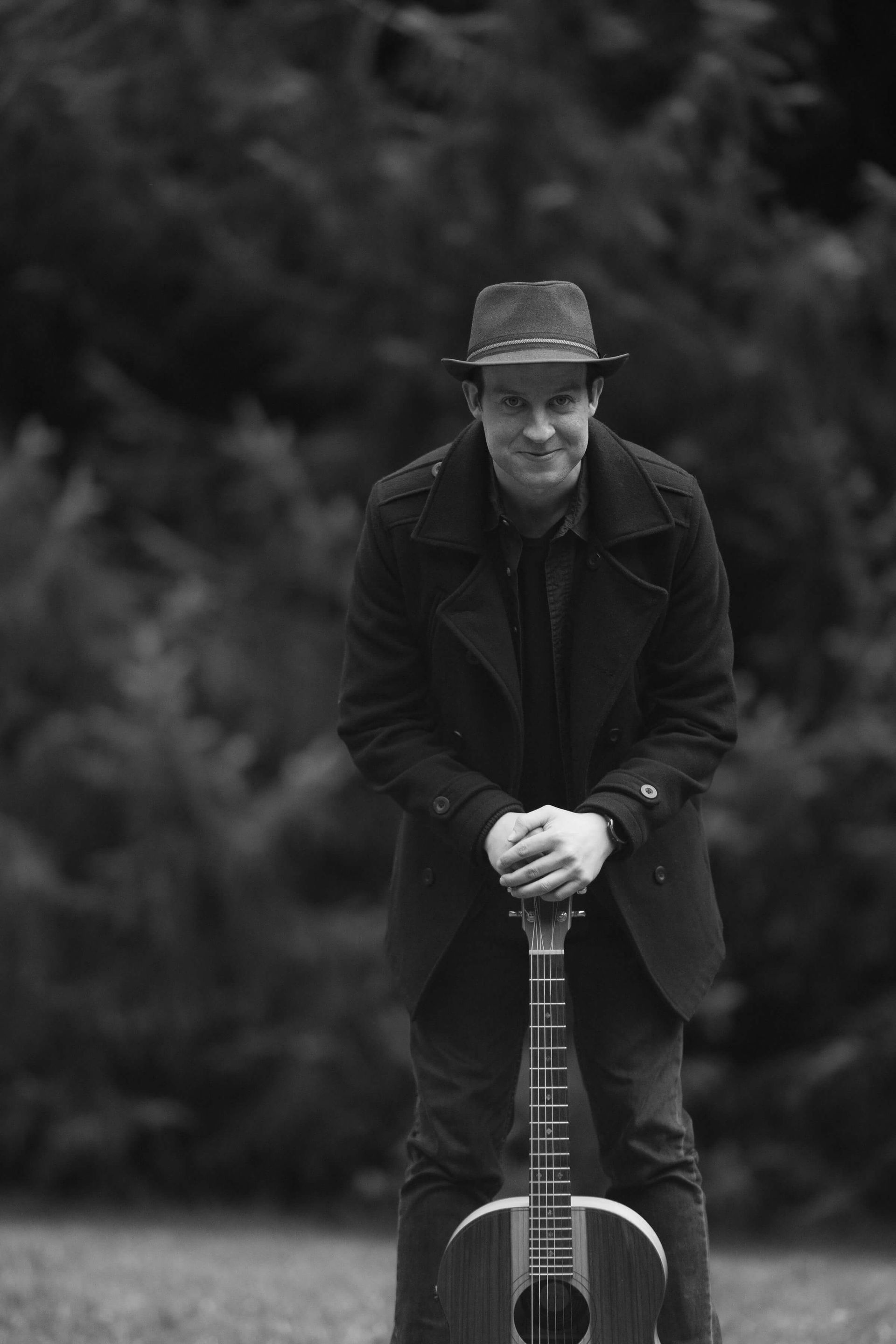 A man in a hat is leaning on a guitar in a black and white photo.