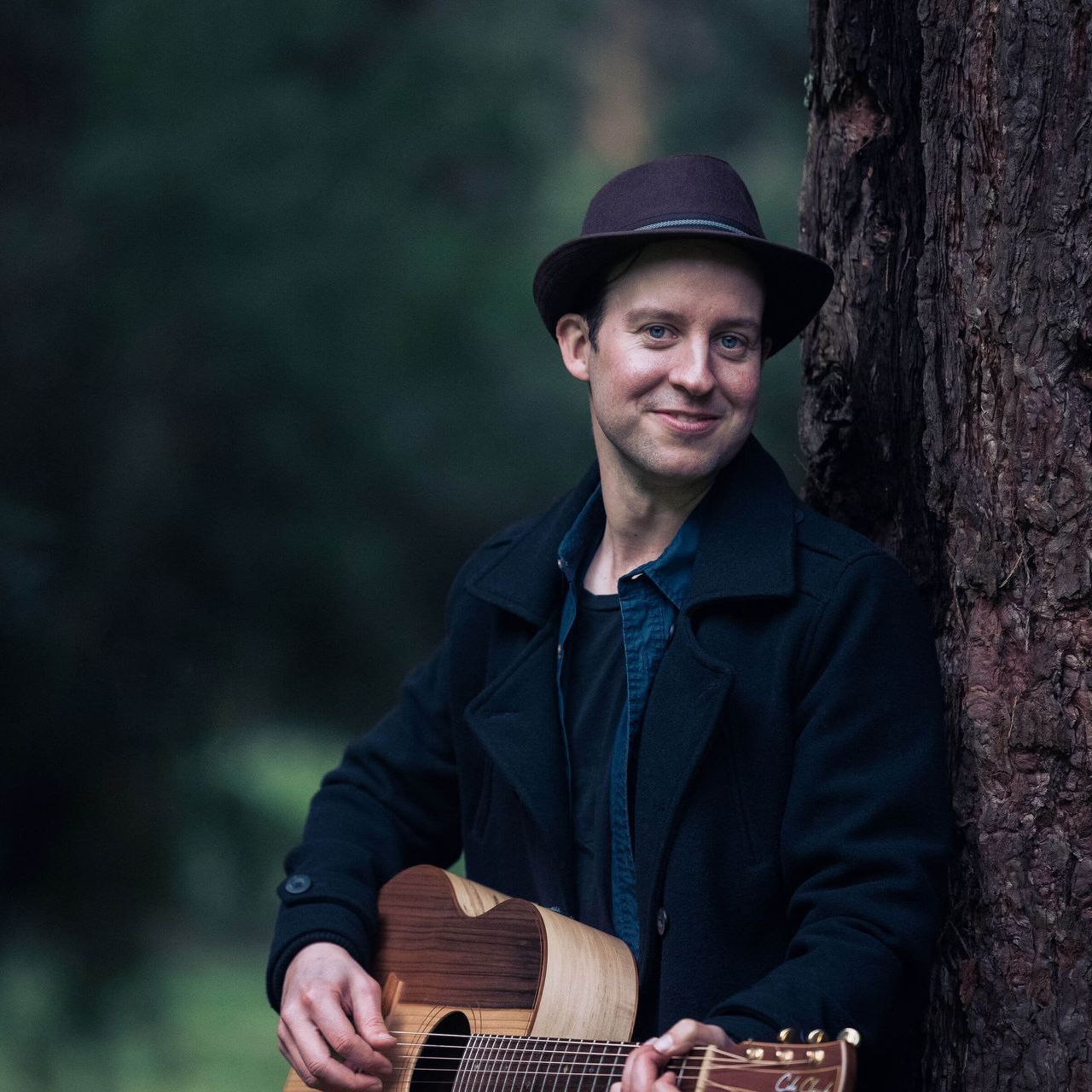 A man leaning against a tree holding a guitar