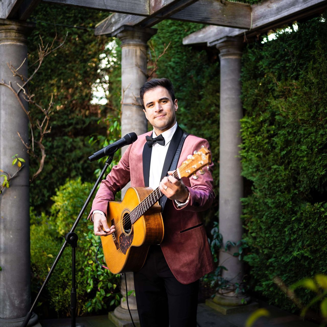 A man in a tuxedo is holding a guitar and singing into a microphone