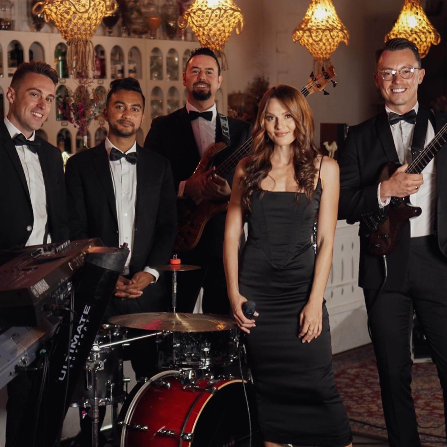 A musical band of six in formal attire, playing instruments with a woman singer in a black dress.