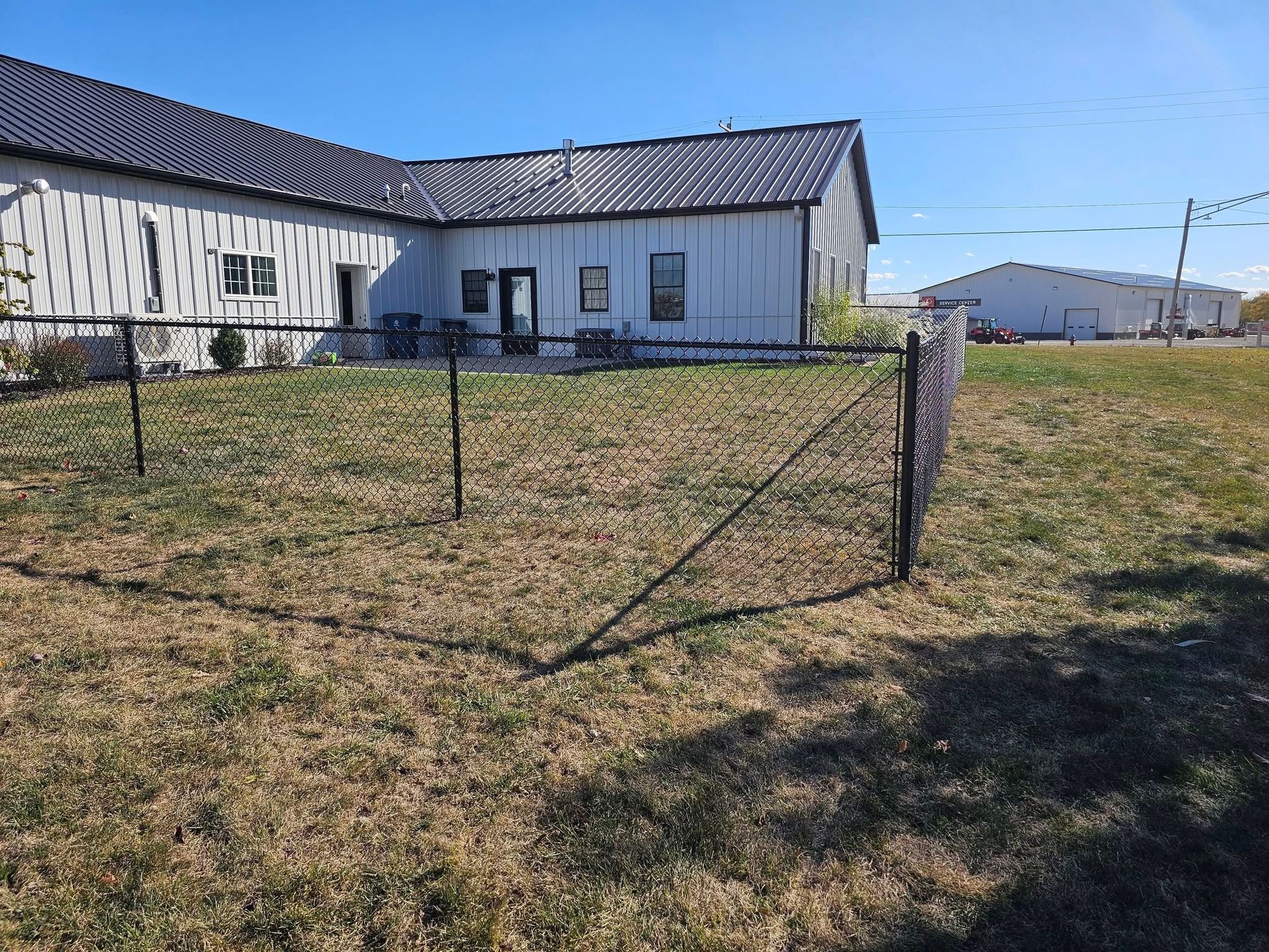 Black chain-link fence in front of a white building with black roof and grass.