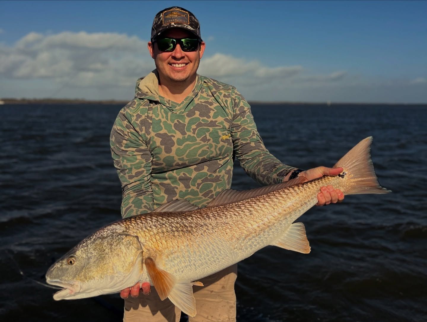 Man holding a large fish on a boat with open water in the background