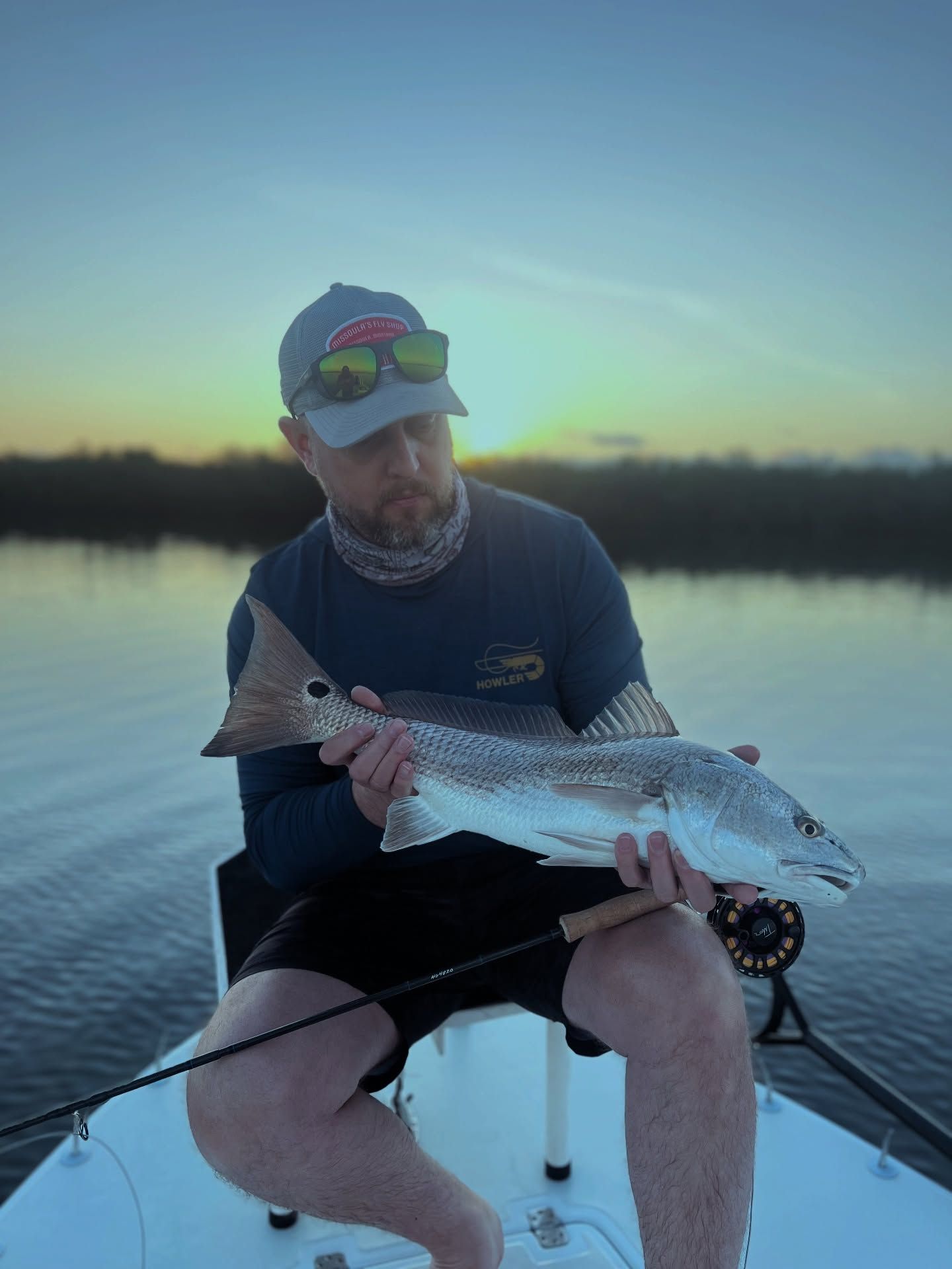 Angler holding a large fish on a boat at dusk on calm water.
