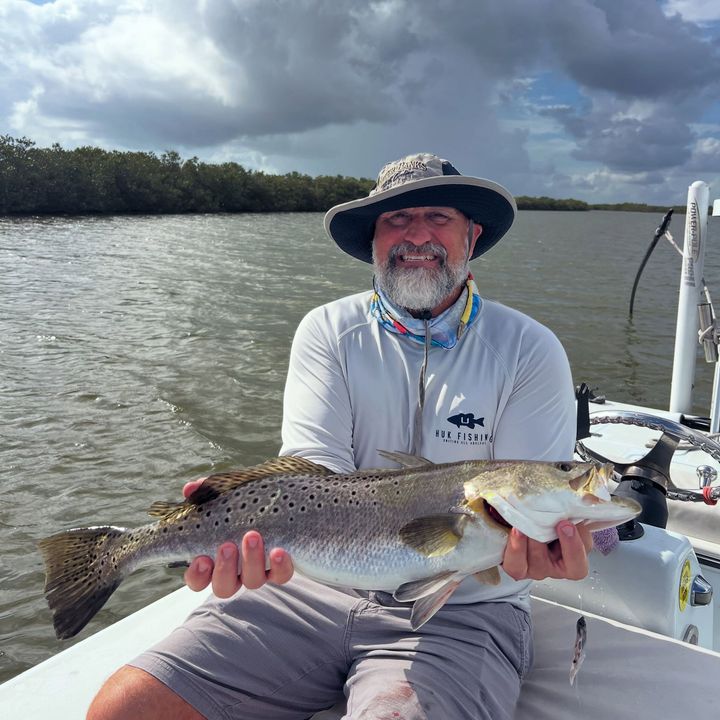 Angler on a boat holds a large fish on a cloudy day in a marshy waterway