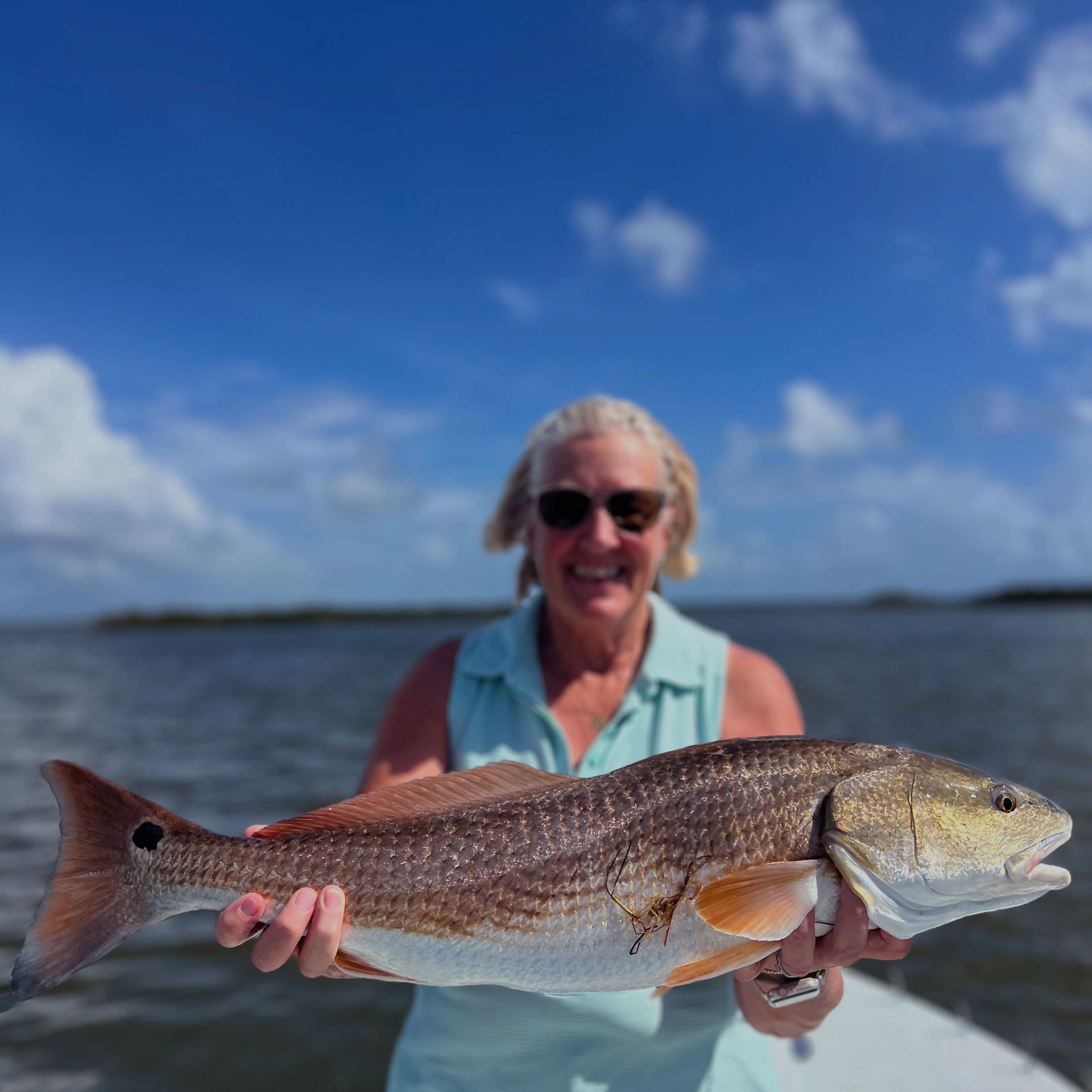 Woman holding a large fish on a boat with water and blue sky behind her