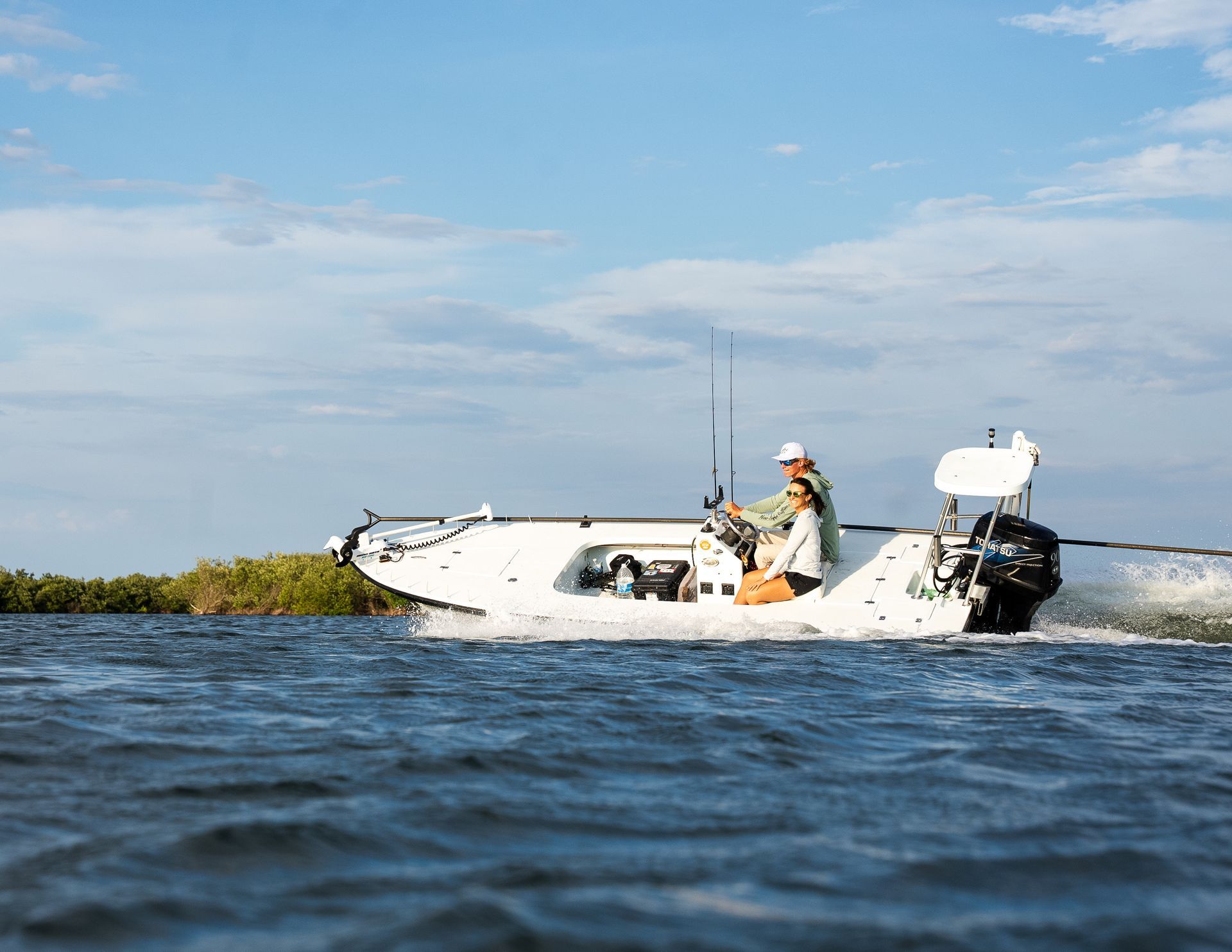 Two people fishing from a white motorboat on calm blue water under a clear sky