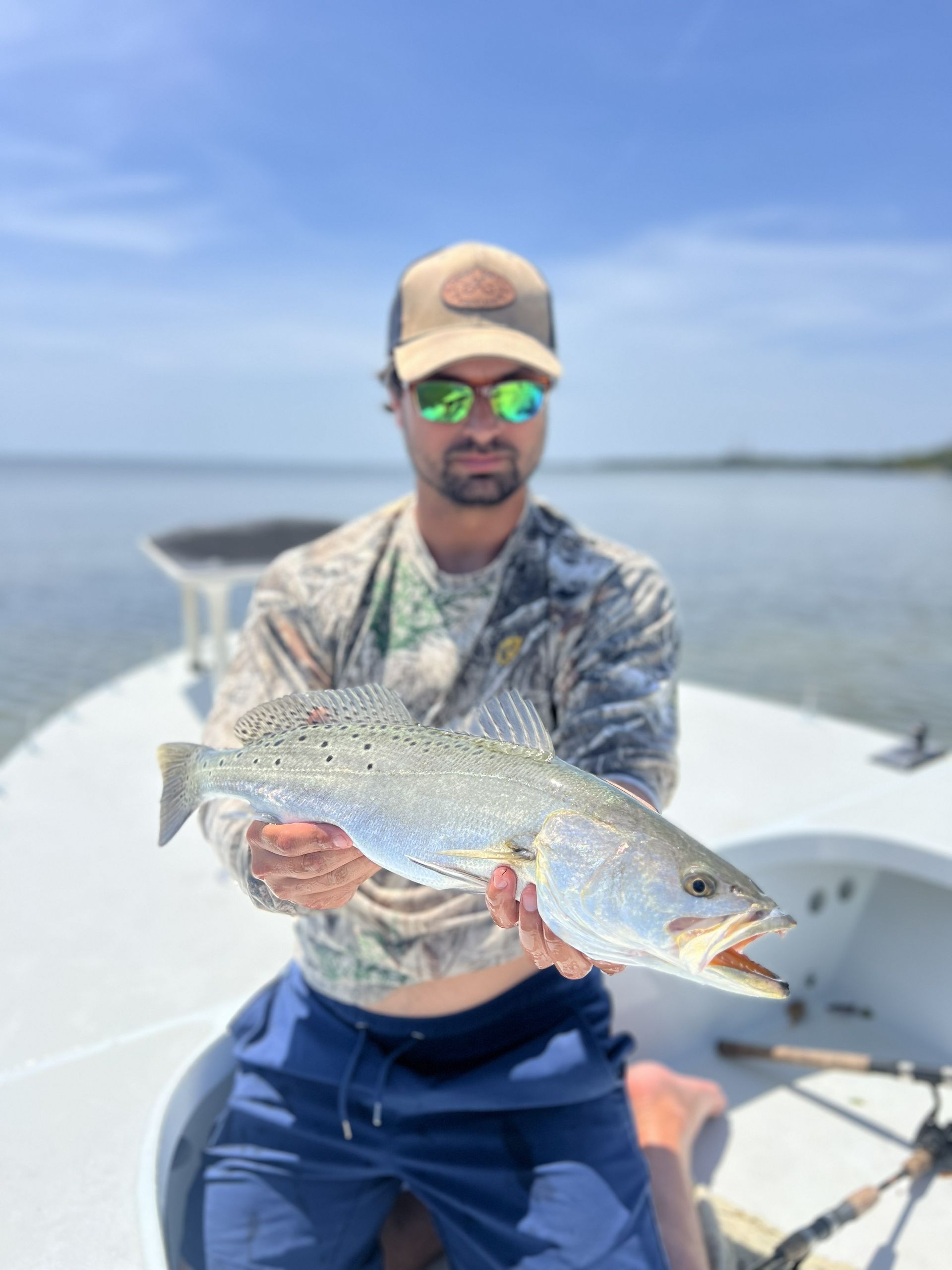 Angler on a boat holding a silver fish over calm water under a bright blue sky