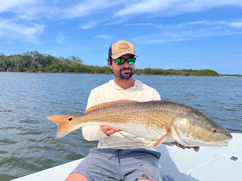Man holding a large fish on a boat in calm water under a blue sky