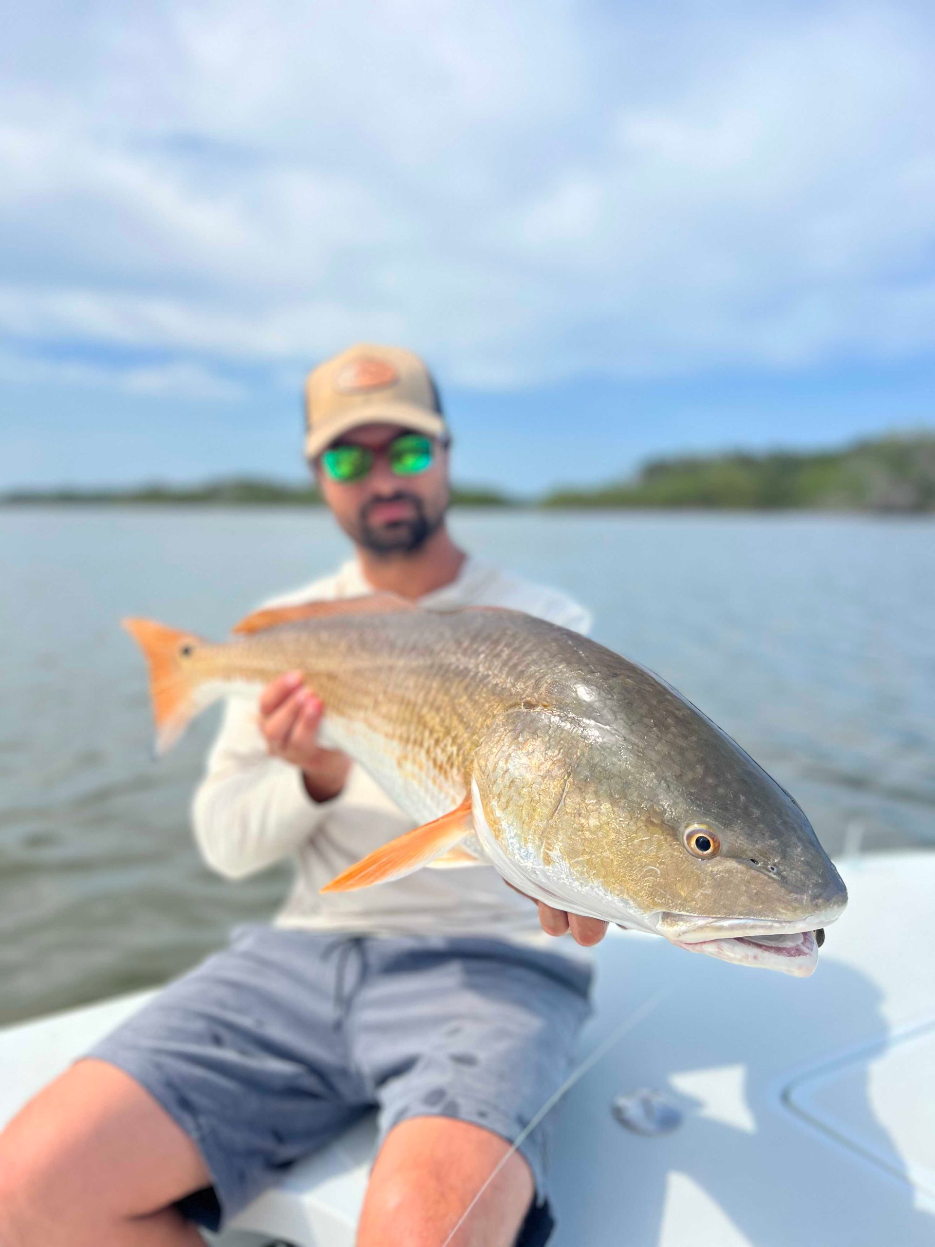 Angler sitting on a boat holding a large silver fish on calm water under a cloudy sky