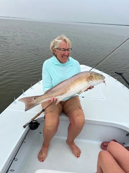 Person on a boat holding a large fish over calm water