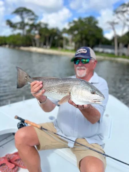 Man holding a large silver fish on a boat, with calm water and shoreline in the background