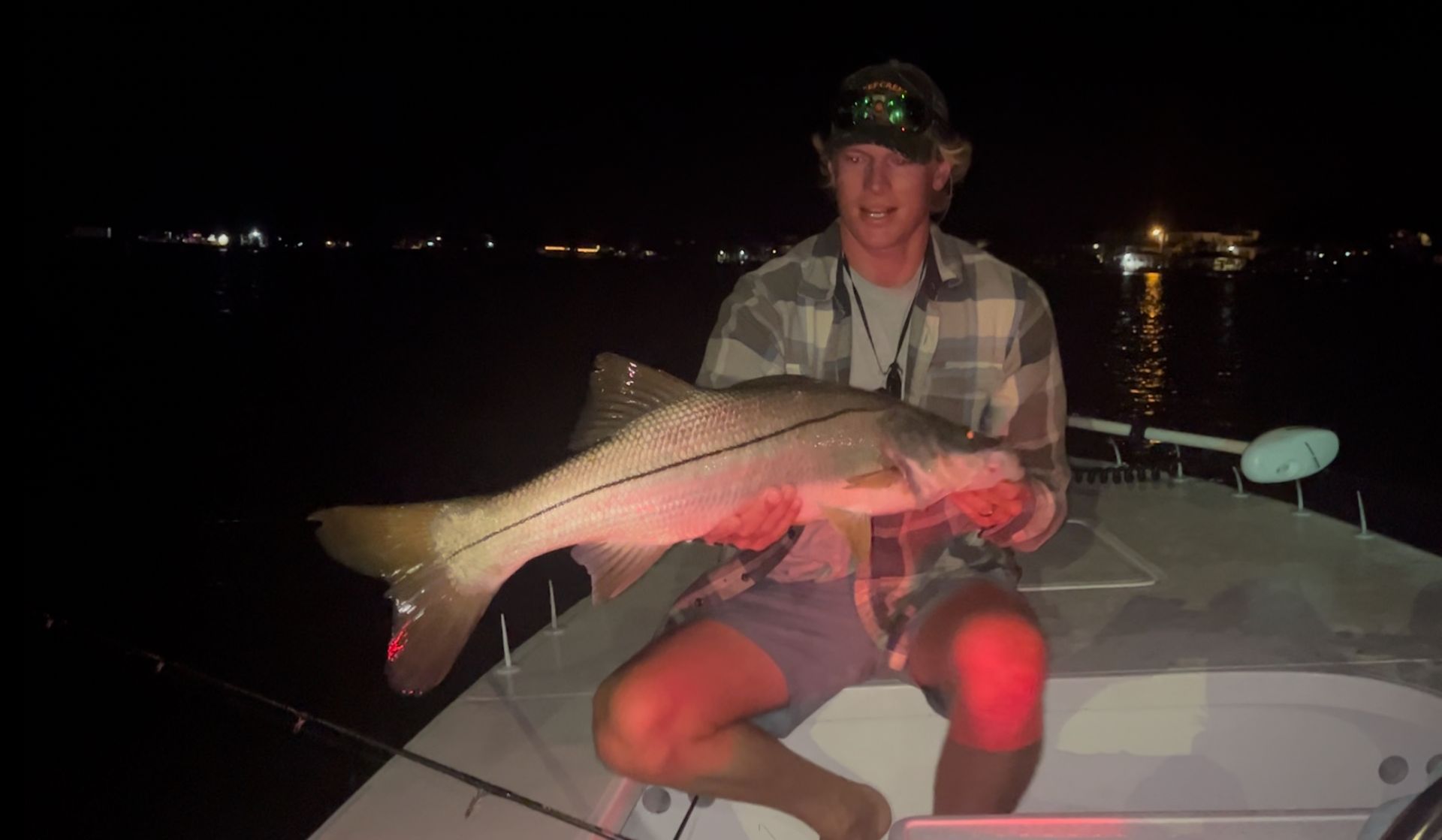 Man holding a large fish on a boat at night, with red light illuminating the scene.