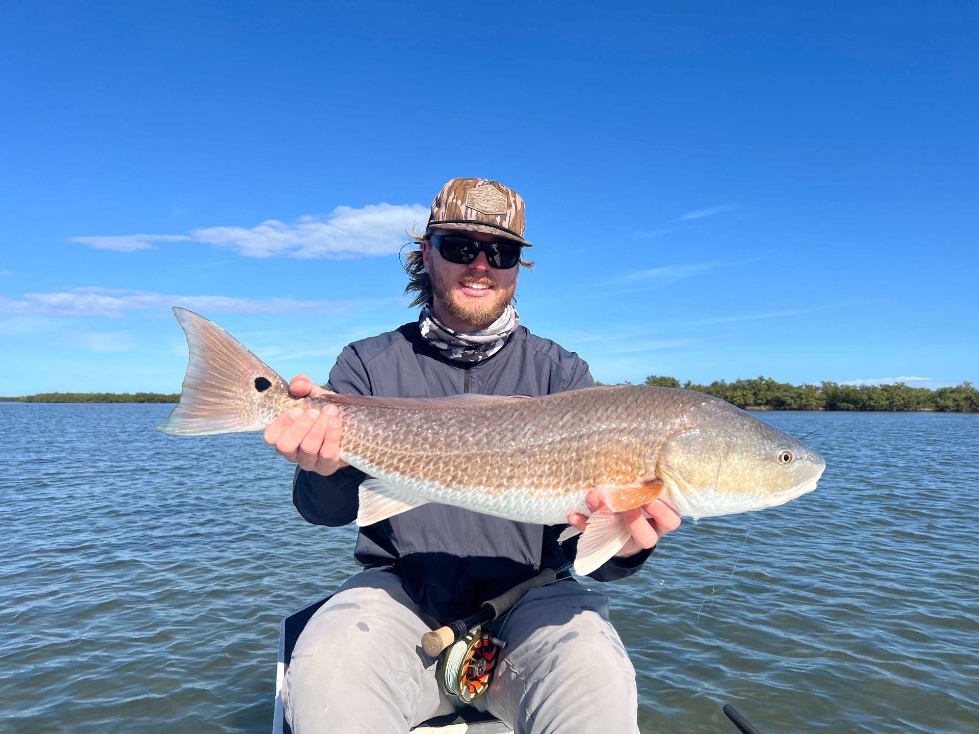 Person holding a large fish on a boat with calm water and blue sky in the background