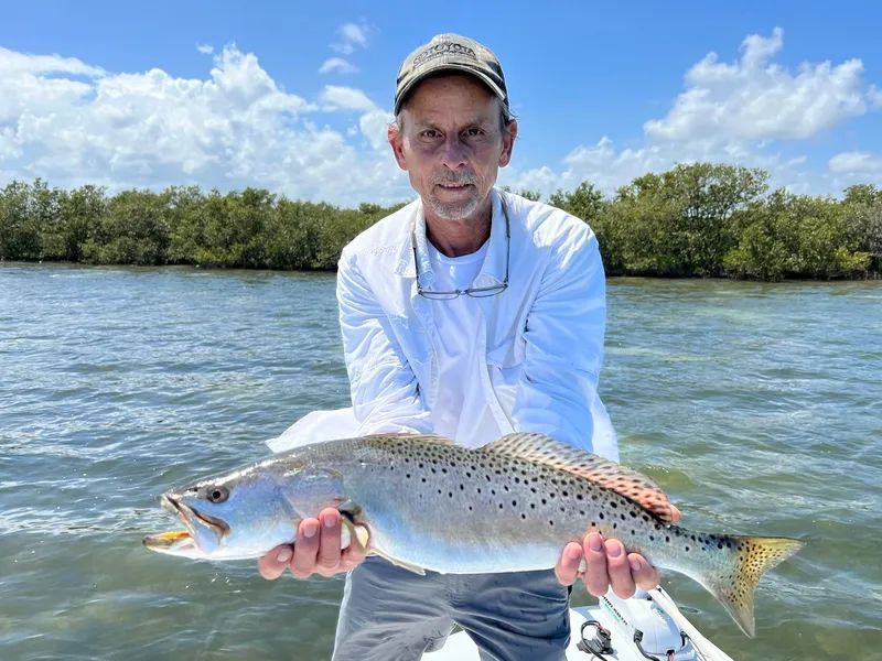 Angler holding a large spotted fish on a boat with mangroves and blue water in the background