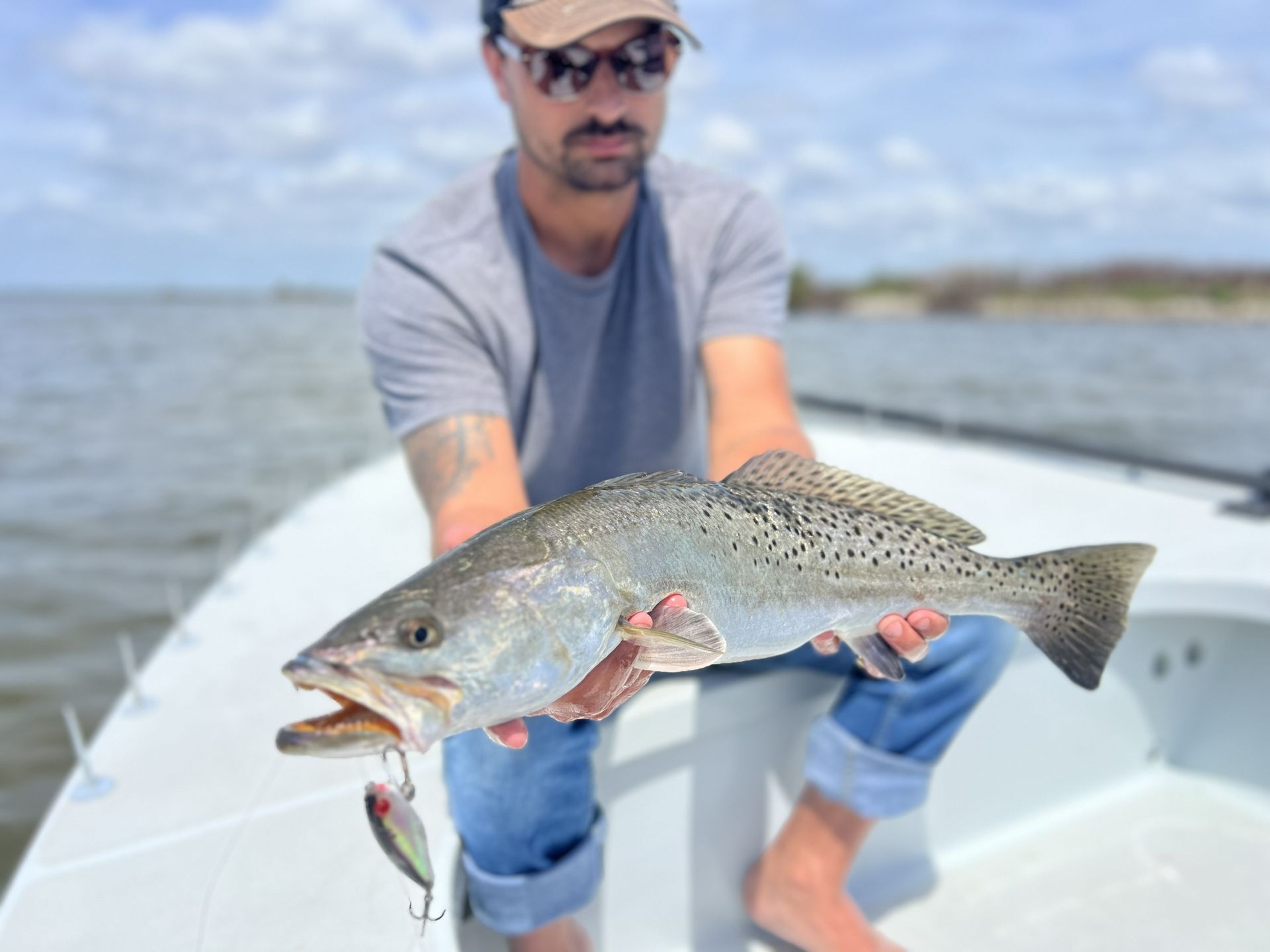 Angler on a boat holds a speckled fish over the water on a sunny day