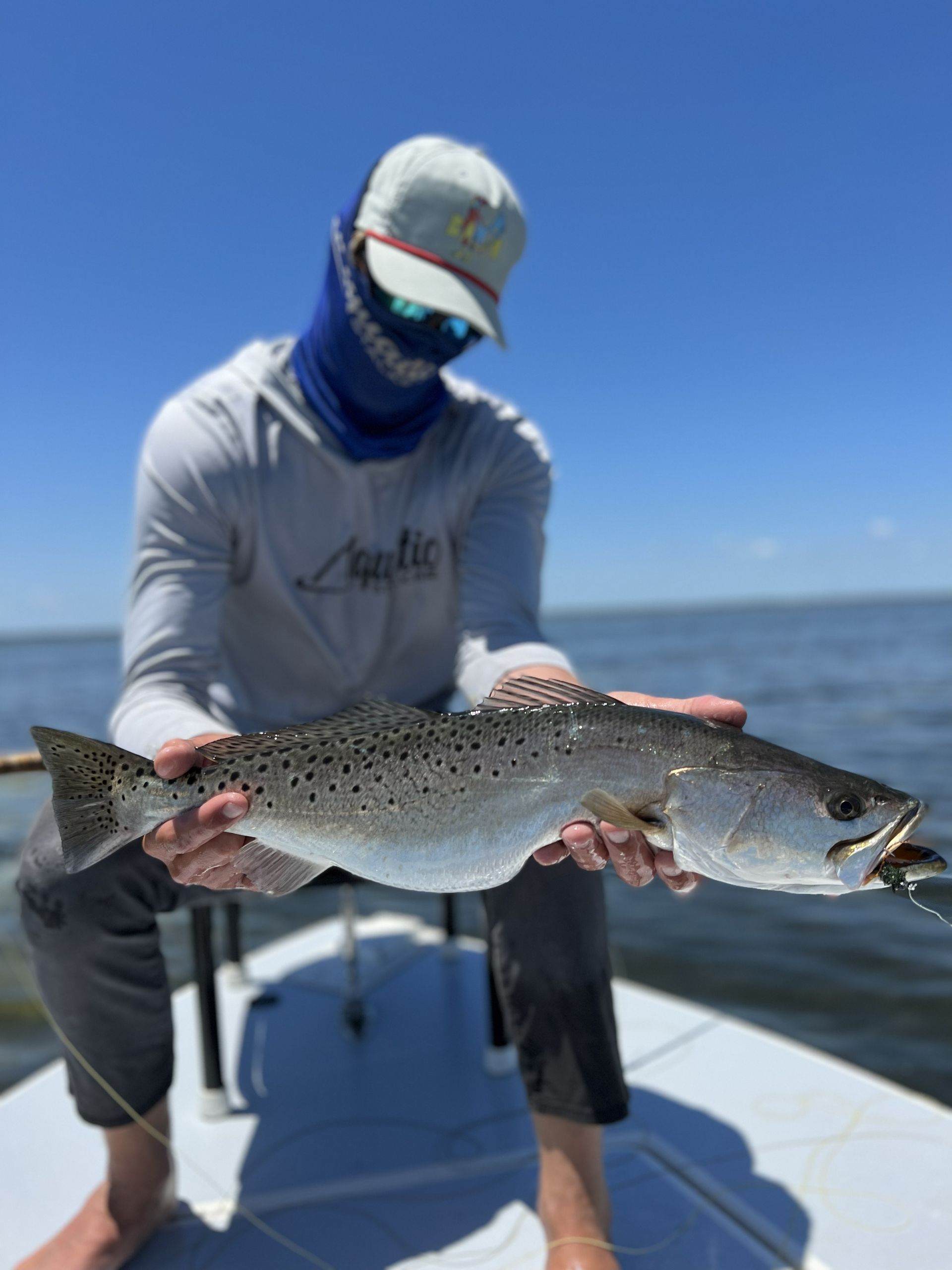 Angler on a boat holding a large speckled fish over open water under a clear blue sky