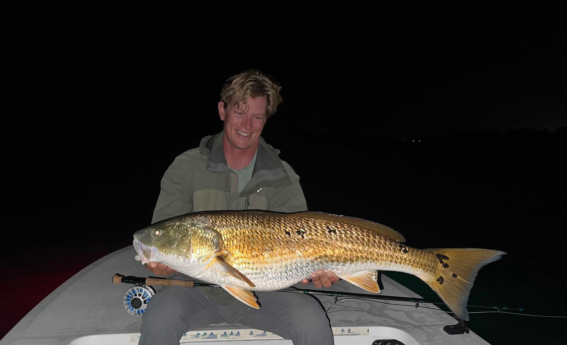 Person holding a large fish on a boat at night.