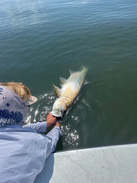 Person holding a large fish in calm water beside a boat