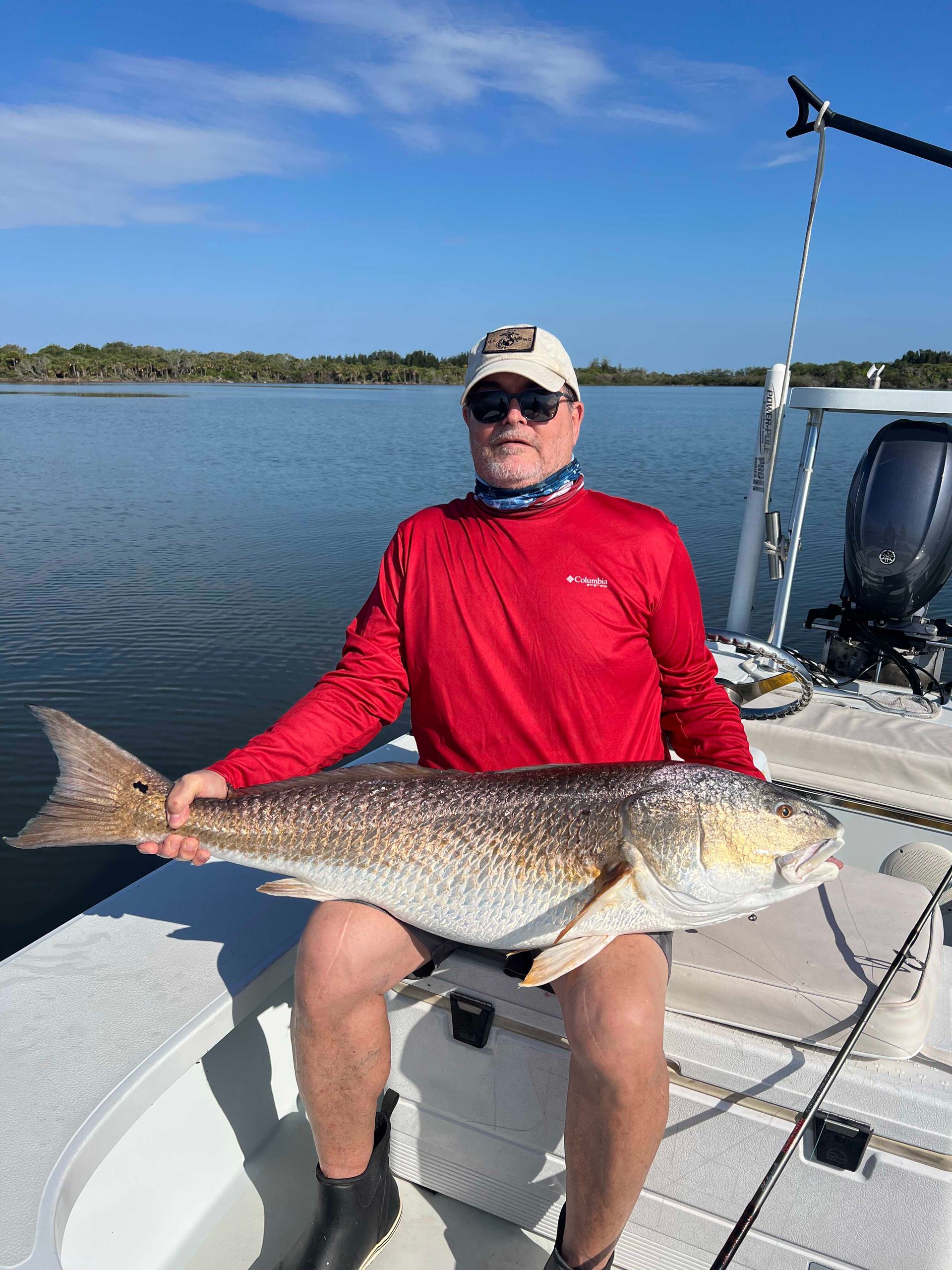 Person in red shirt holds a large fish on a boat on calm water under a clear blue sky
