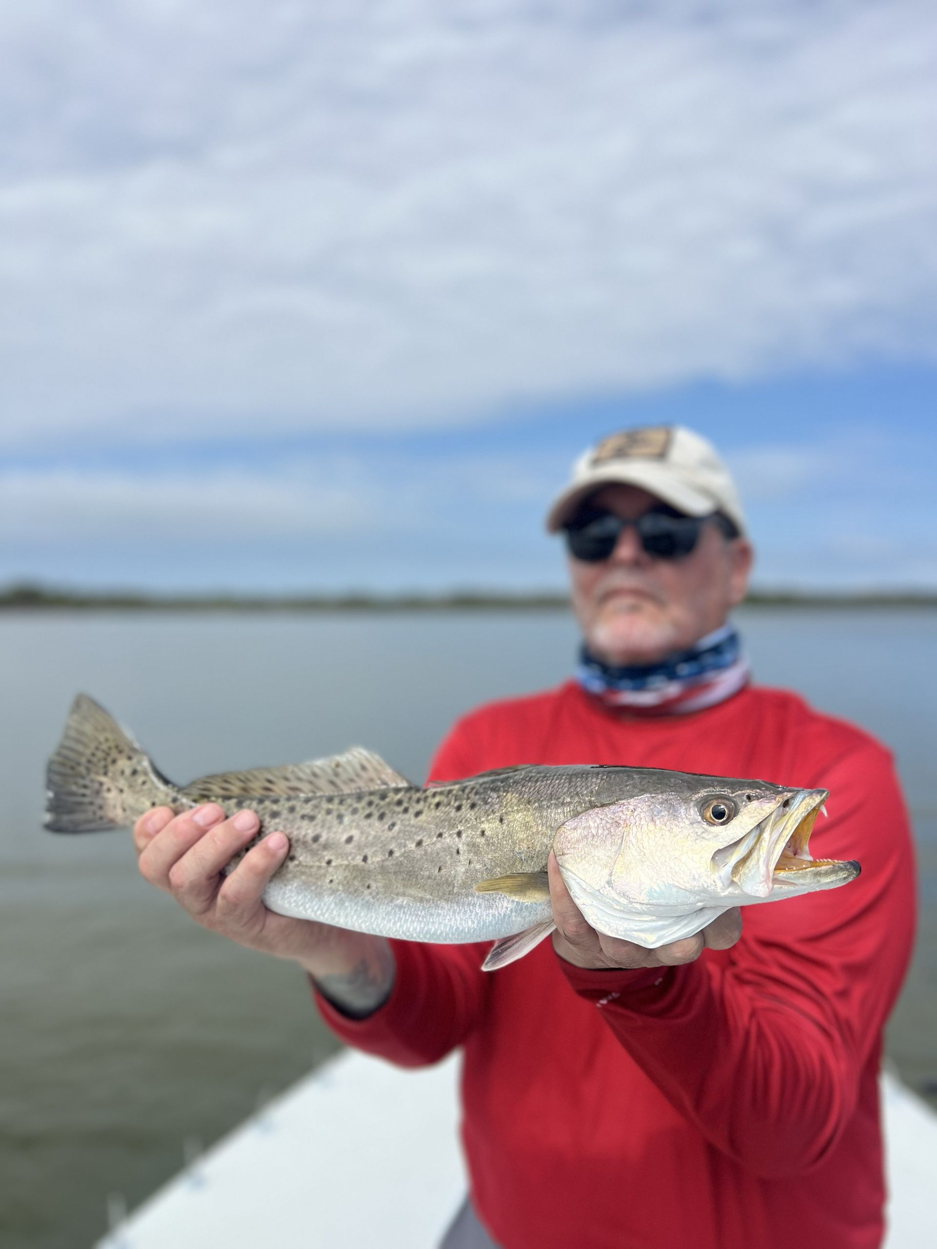 Angler in red shirt holding a speckled fish on a boat against a cloudy lake backdrop