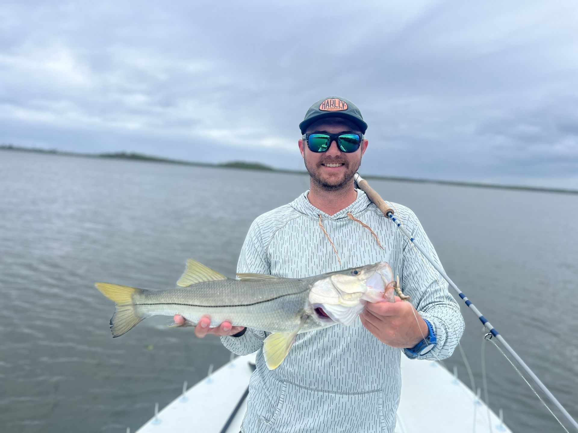 Man holding a silver fish on a boat, with calm water and cloudy sky in the background