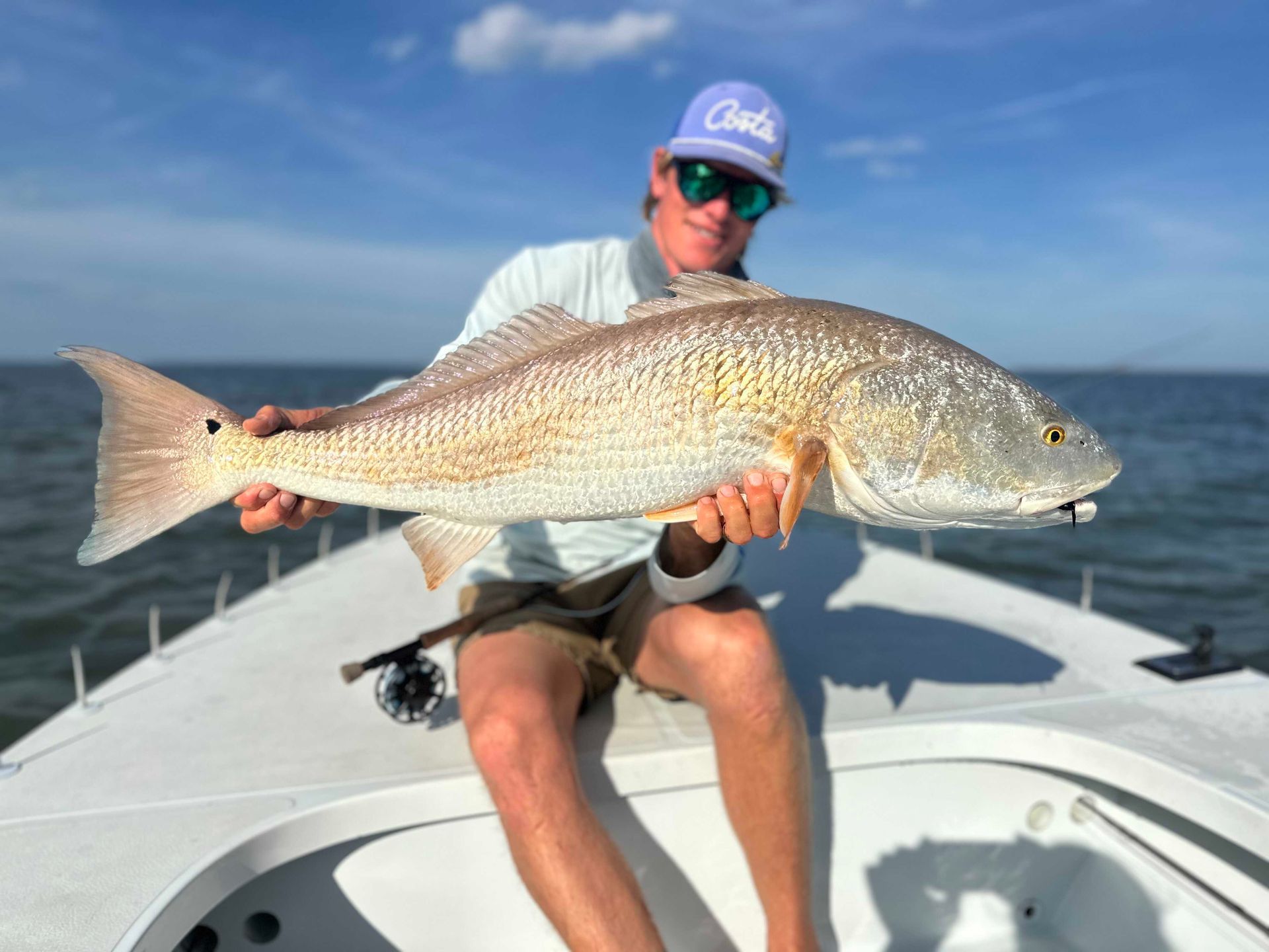 Angler holding a large redfish on a boat under a blue sky