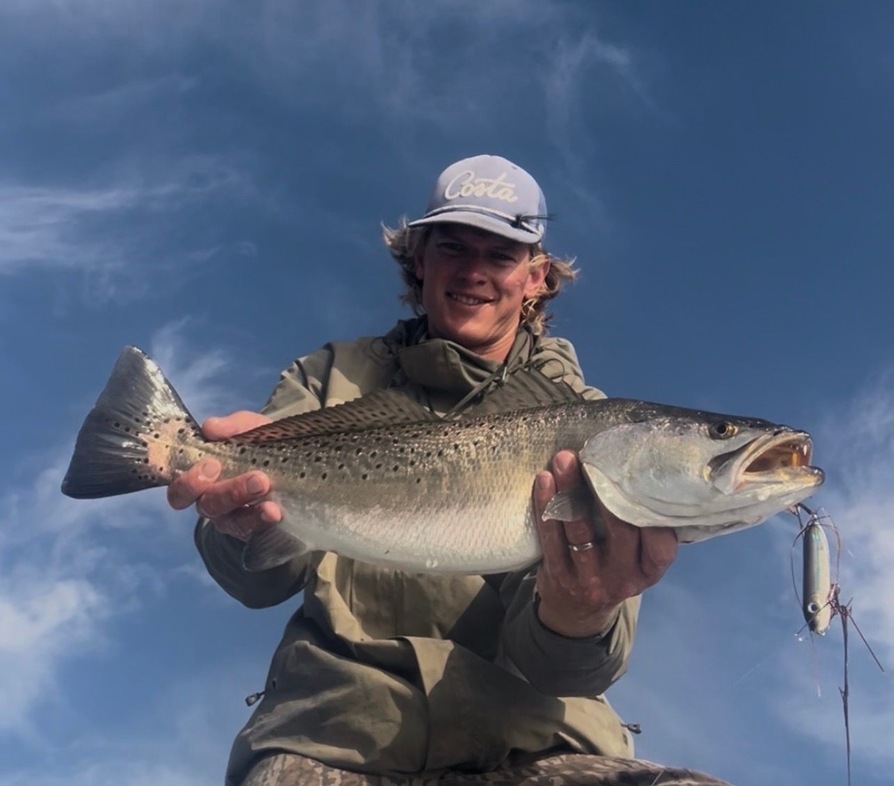 Angler holding a large fish on a boat against a blue sky
