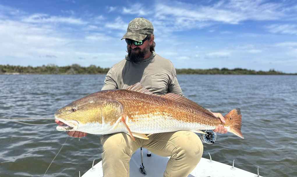 Angler holding a large redfish on a boat on calm water under a blue sky