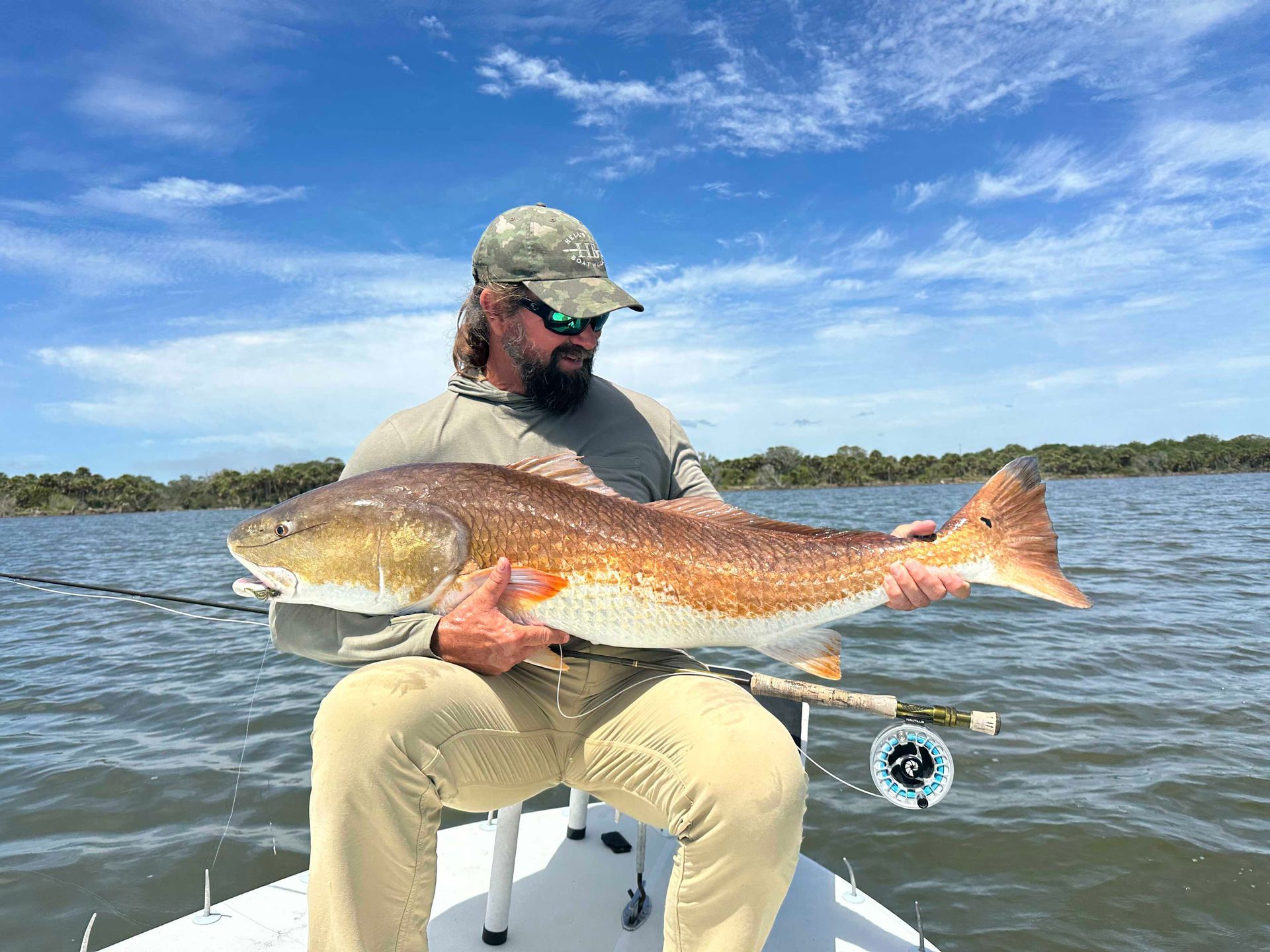 Angler holding a large red fish on a boat in calm water under a blue sky