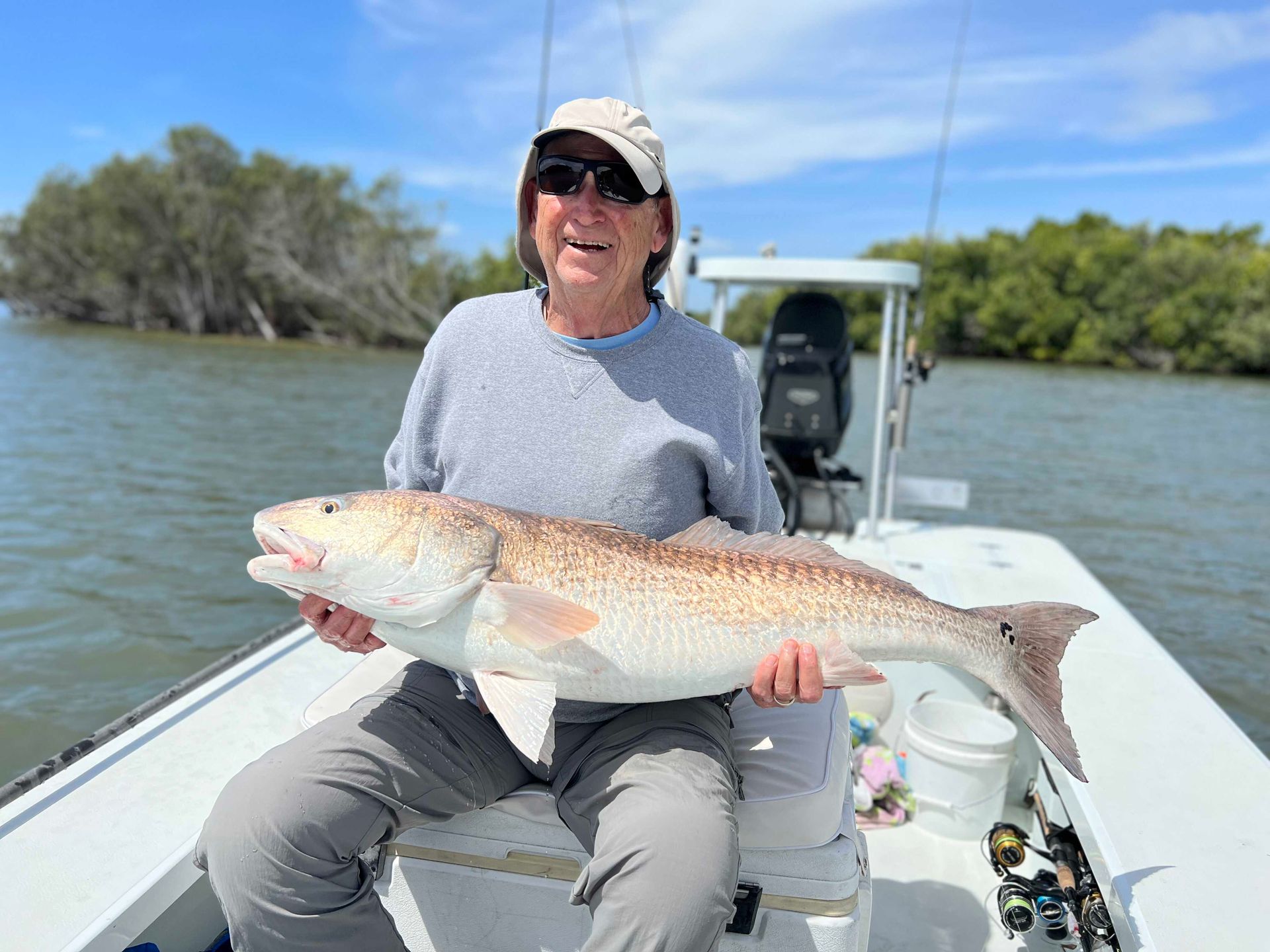 Angler sitting on a boat holding a large fish on a sunny river or bay.