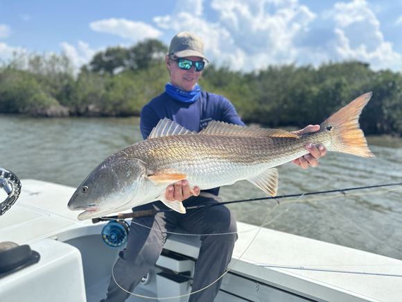 Angler holding a large redfish on a boat in a sunny marshland setting