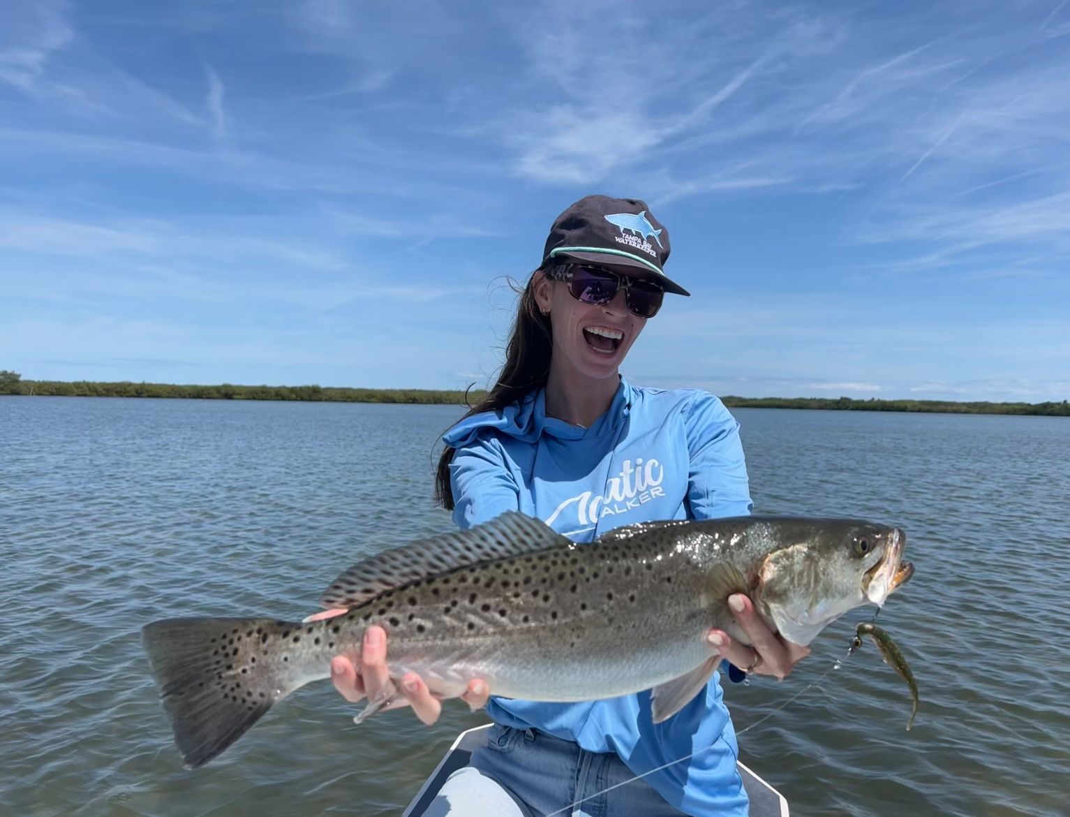 Person holding a large speckled fish on a boat under a blue sky on calm water