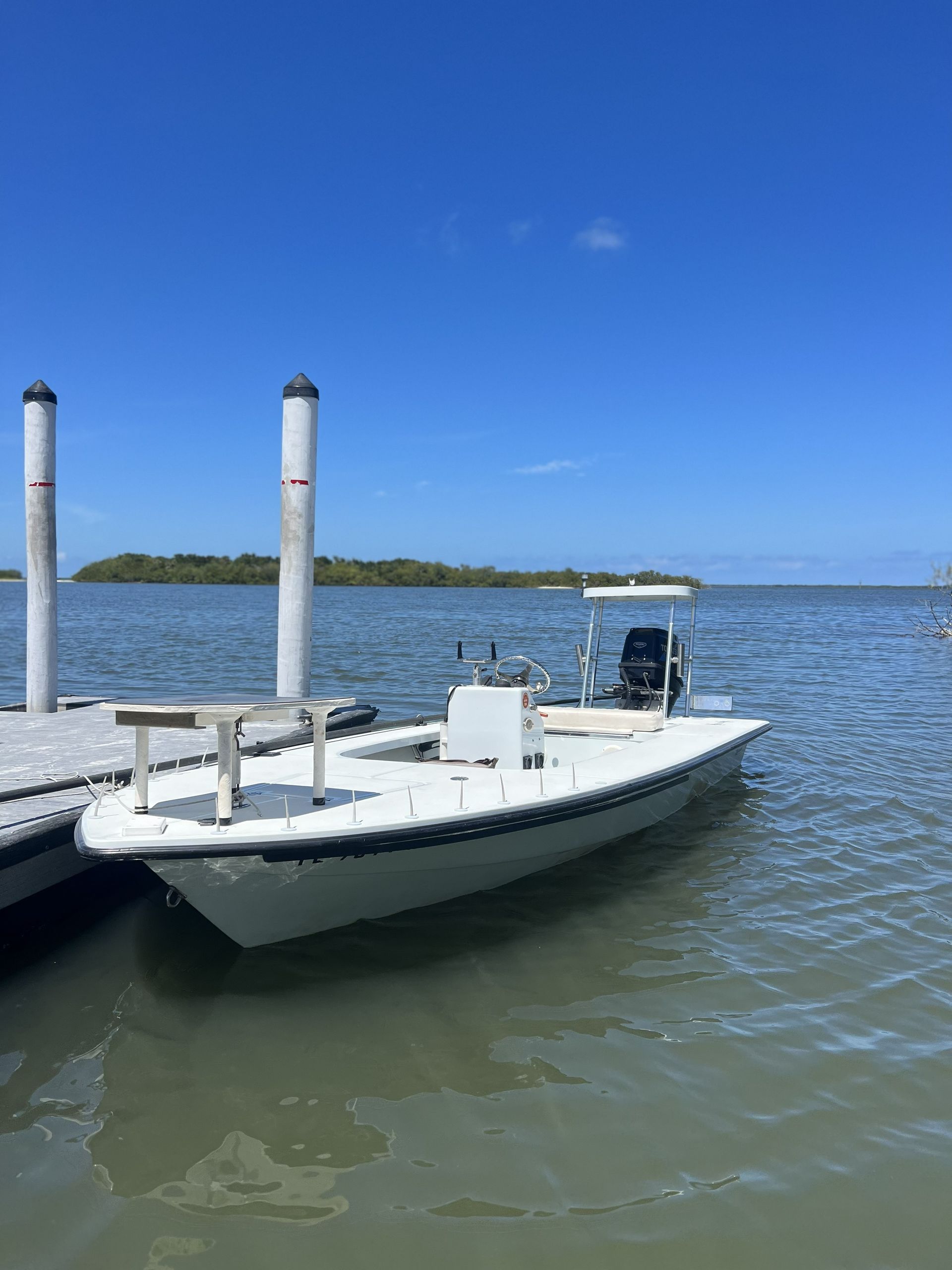 Small white motorboat tied to a dock on calm water under a clear blue sky.