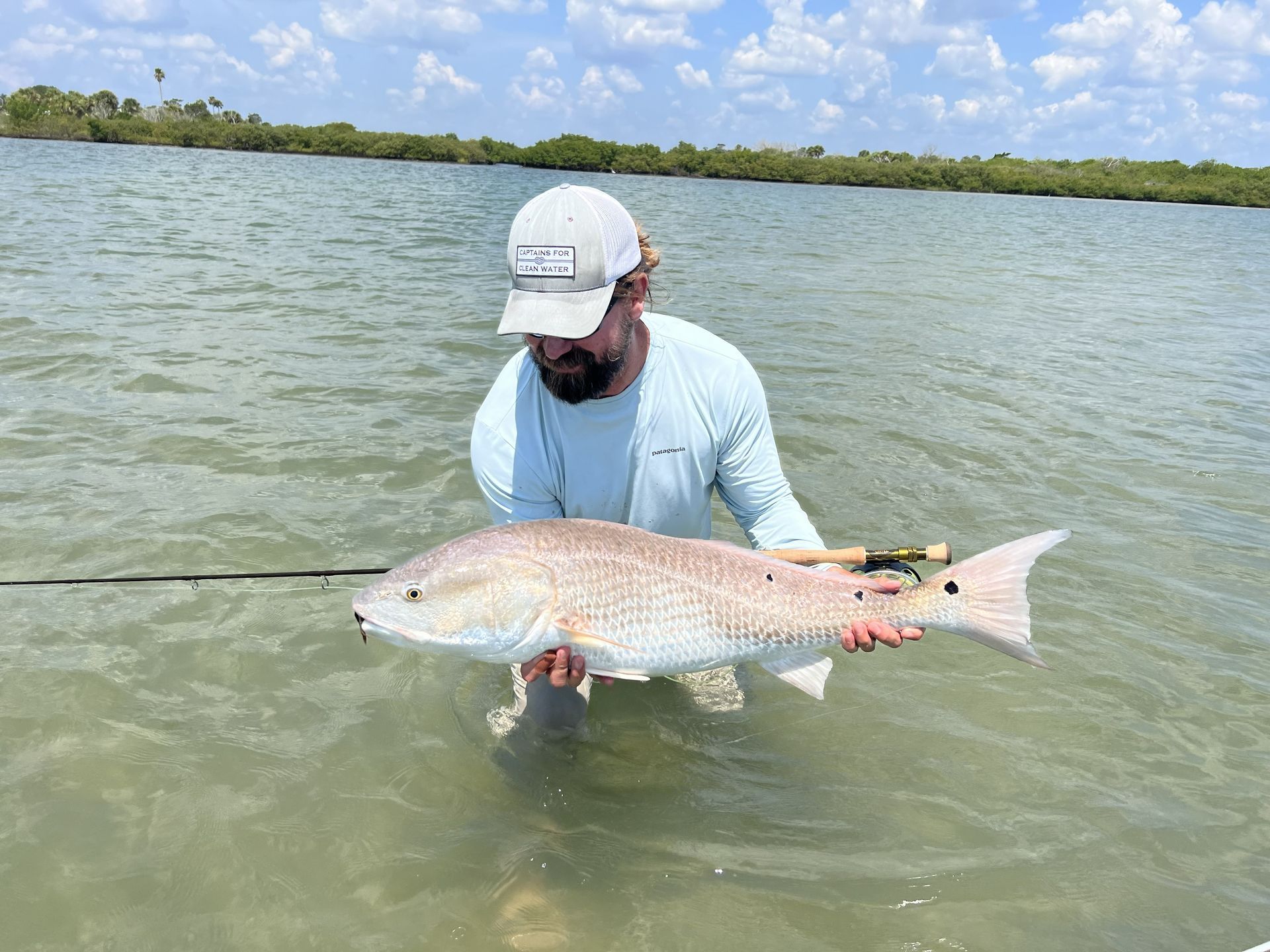Angler holding a large spotted fish in shallow water under a cloudy sky
