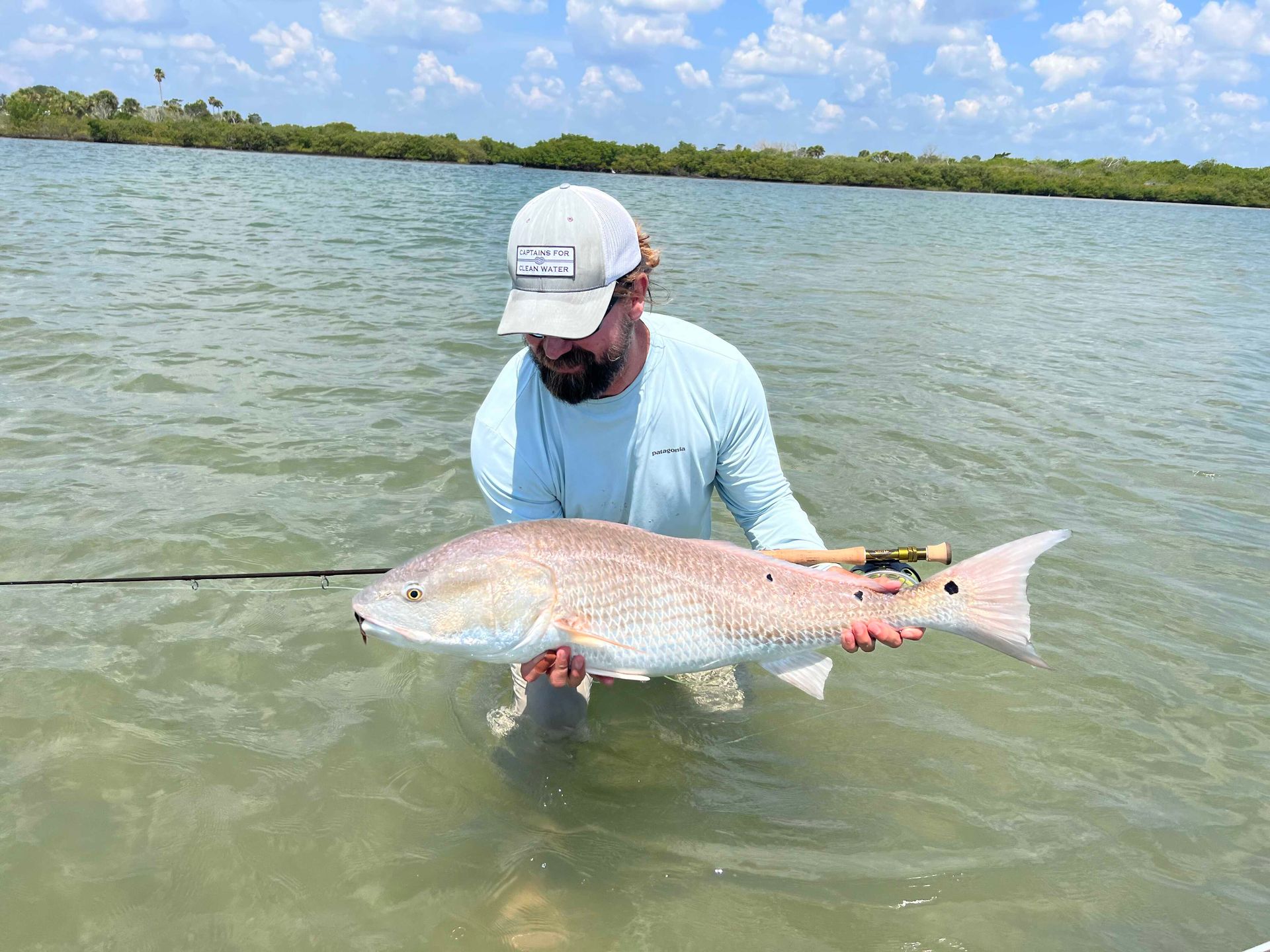 Person holding a large fish while standing in shallow water near a shoreline
