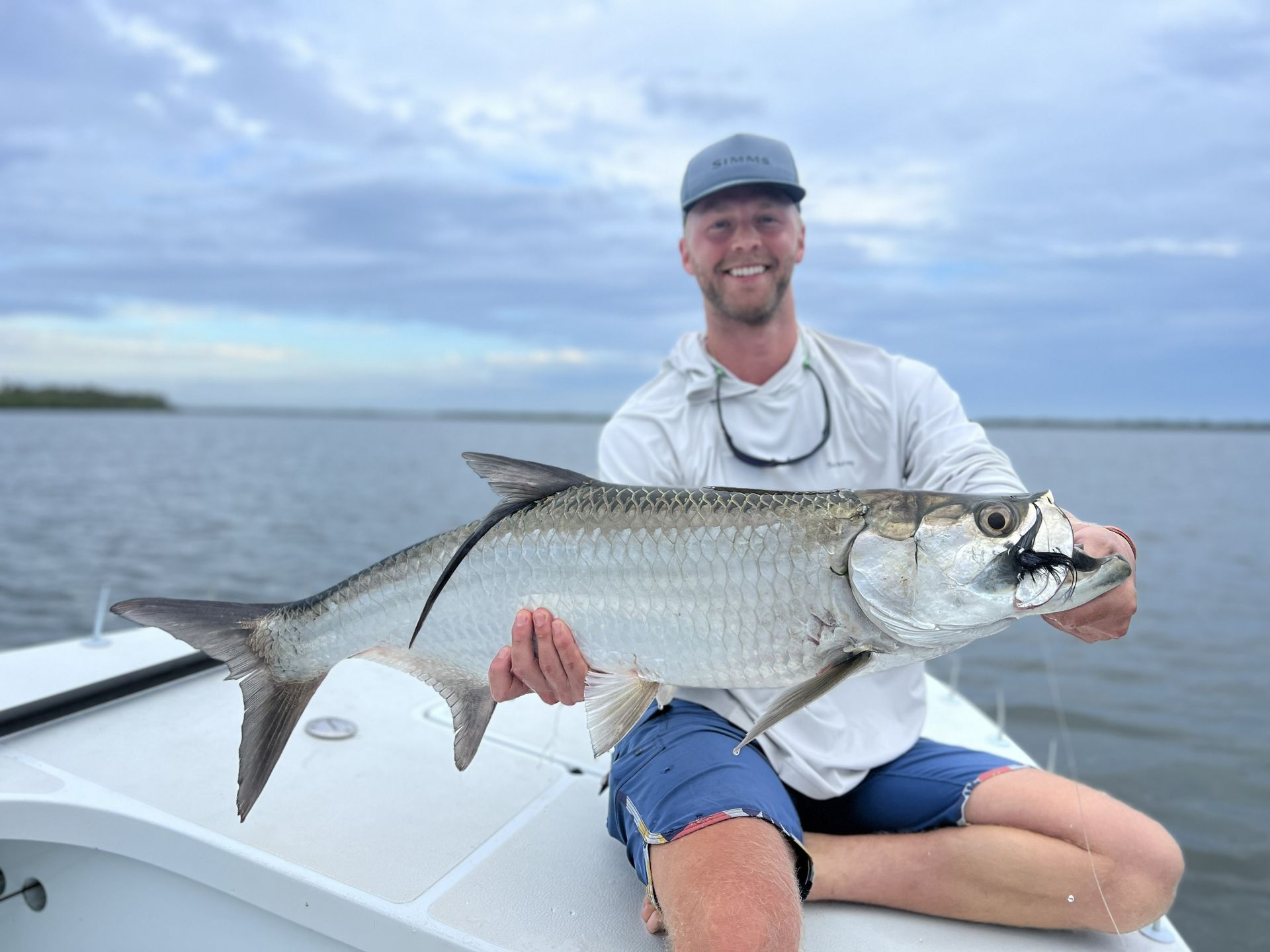Man holding a large silver fish on a boat under a cloudy sky