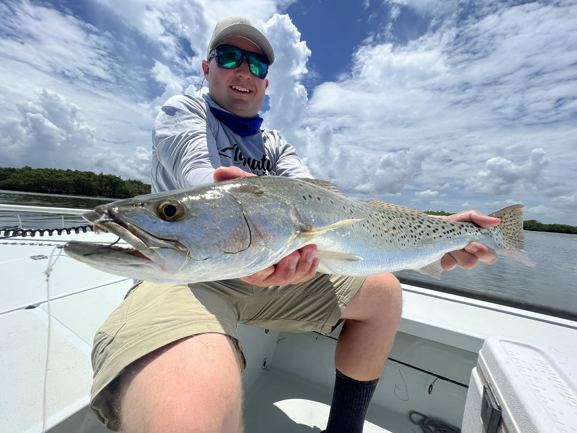 Angler on a boat holding a large silver fish under a cloudy sky
