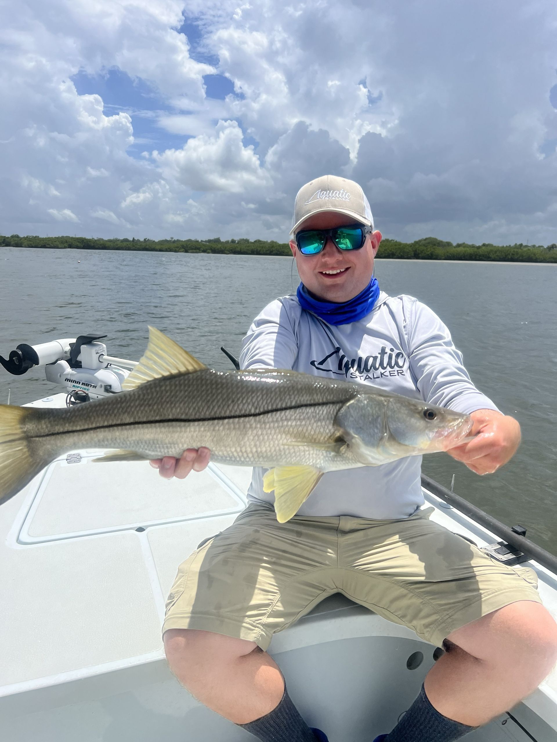 Person on a boat holding a large fish under a cloudy sky and wearing sunglasses.