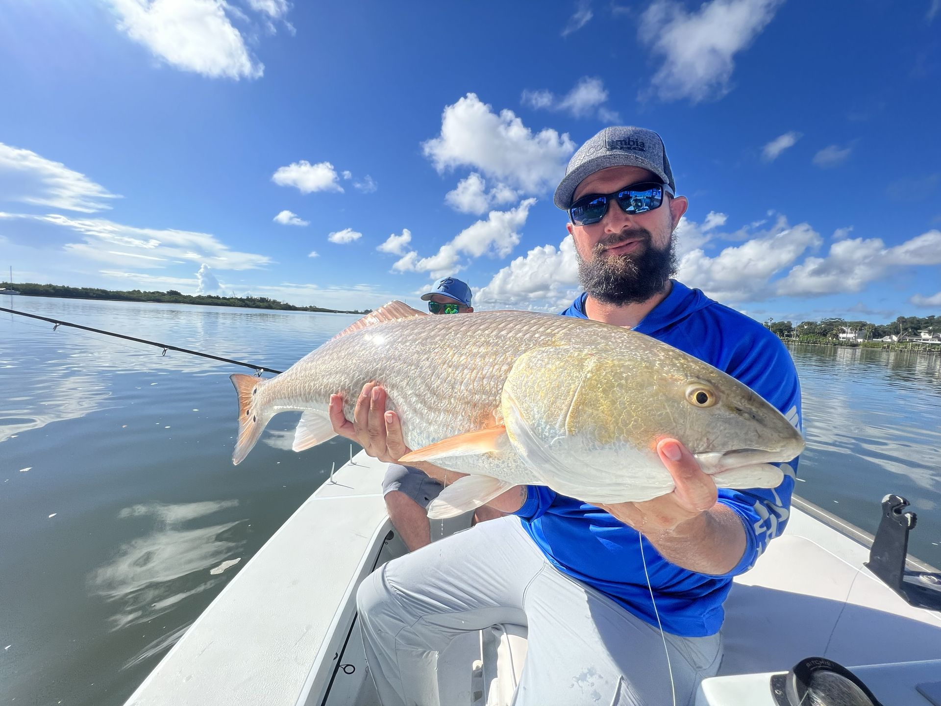 Man on a boat holding a large silver fish on a sunny lake